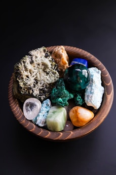 A wooden bowl contains various colorful gemstones.