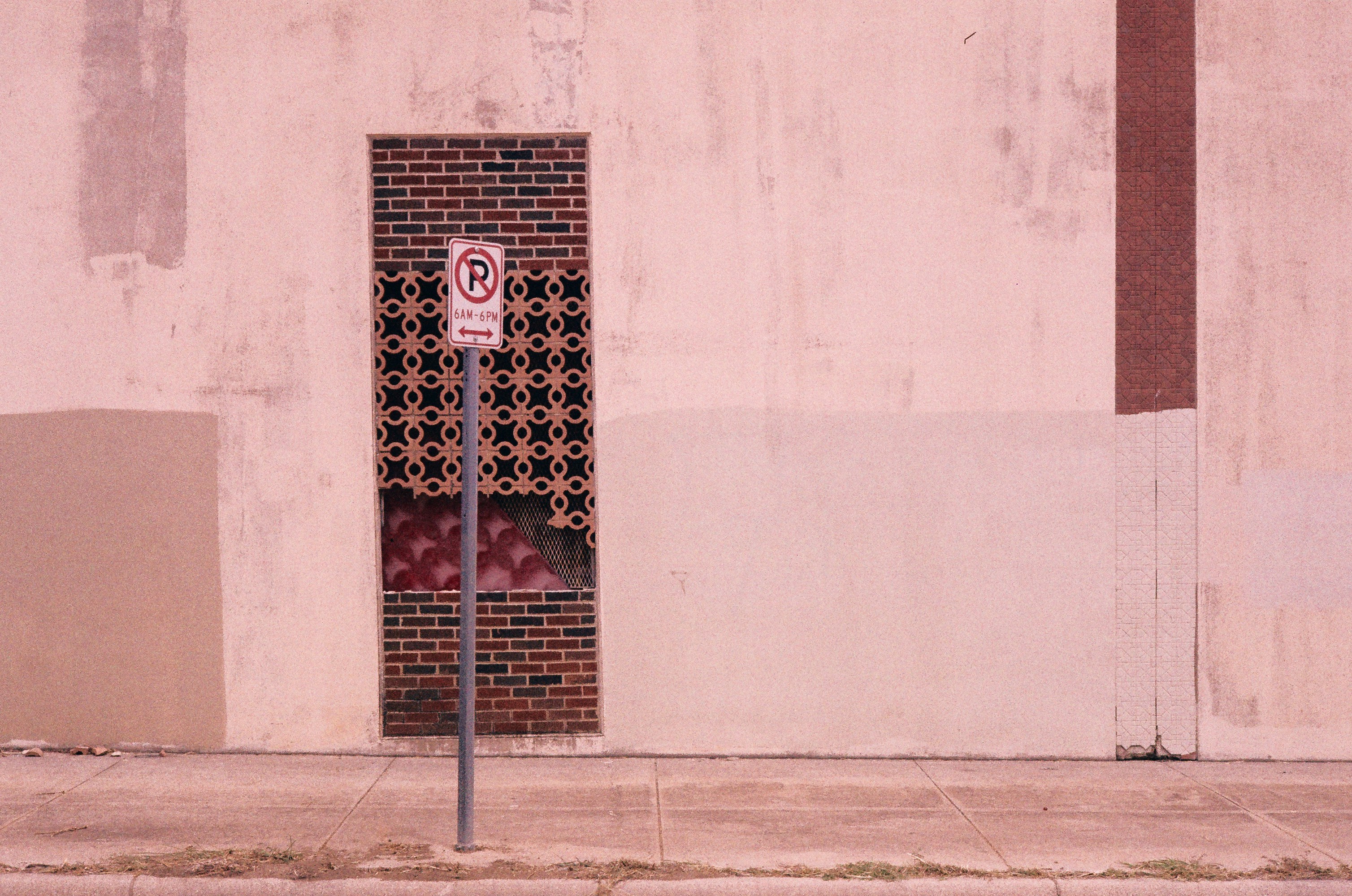 A decorative brick-framed window with ornate metal screening, punctuated by a no parking sign. Shot on Shanghai Color Film 400.