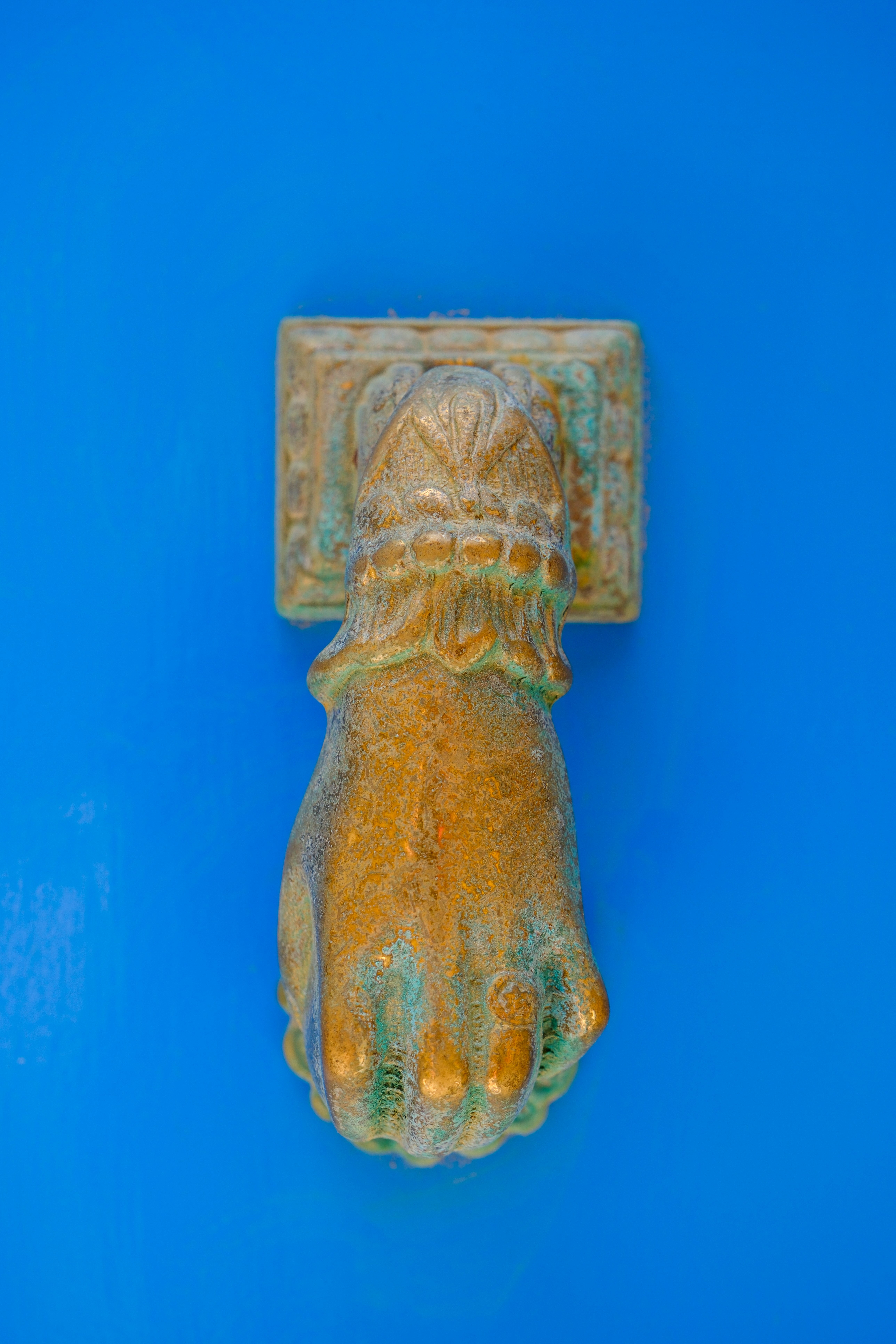 A bronze hand door knocker is mounted on blue.
