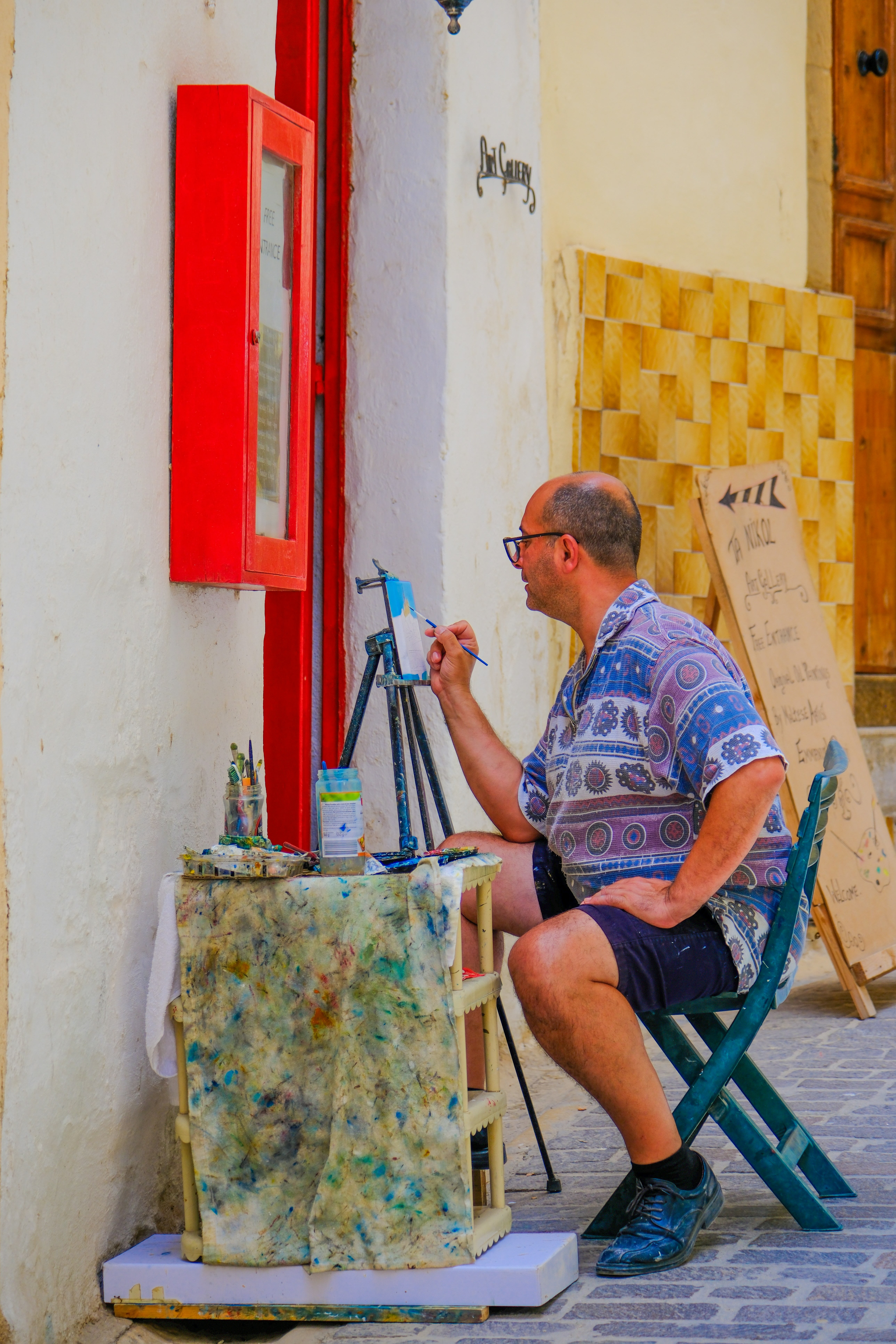An artist paints outdoors with a small easel.