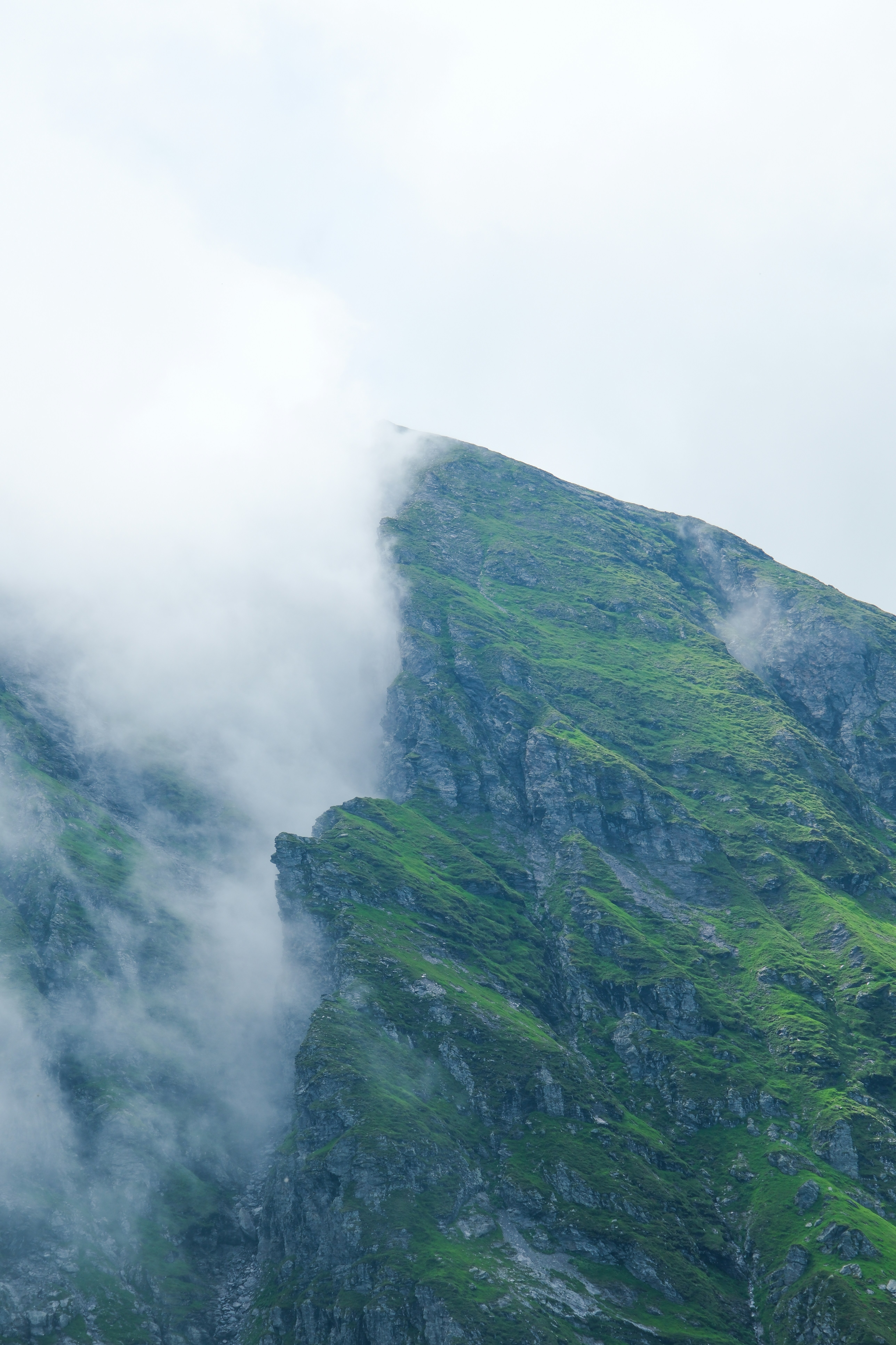 A green mountain peeks through the clouds.