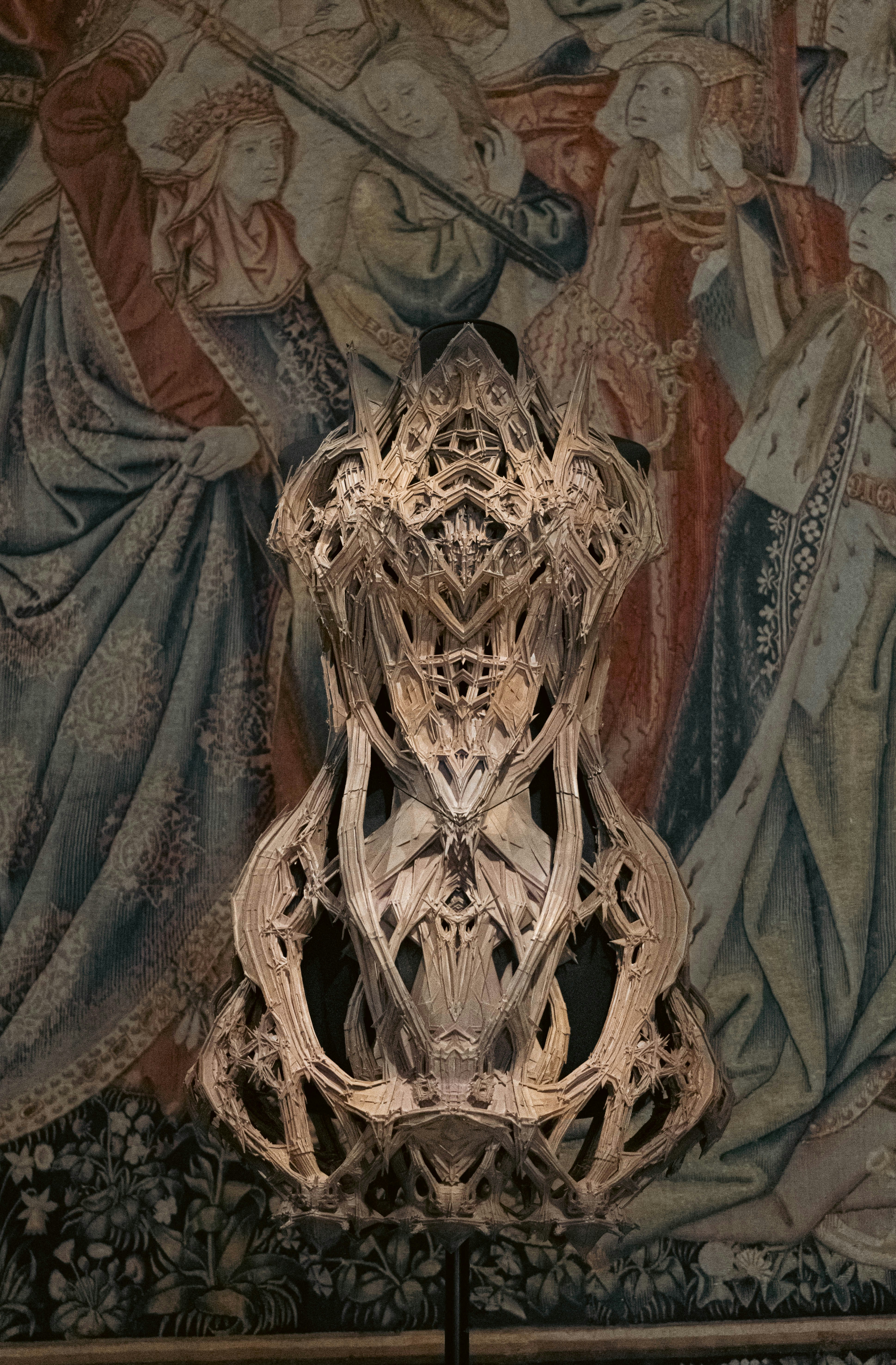 An intricate sculpture is displayed against a tapestry.