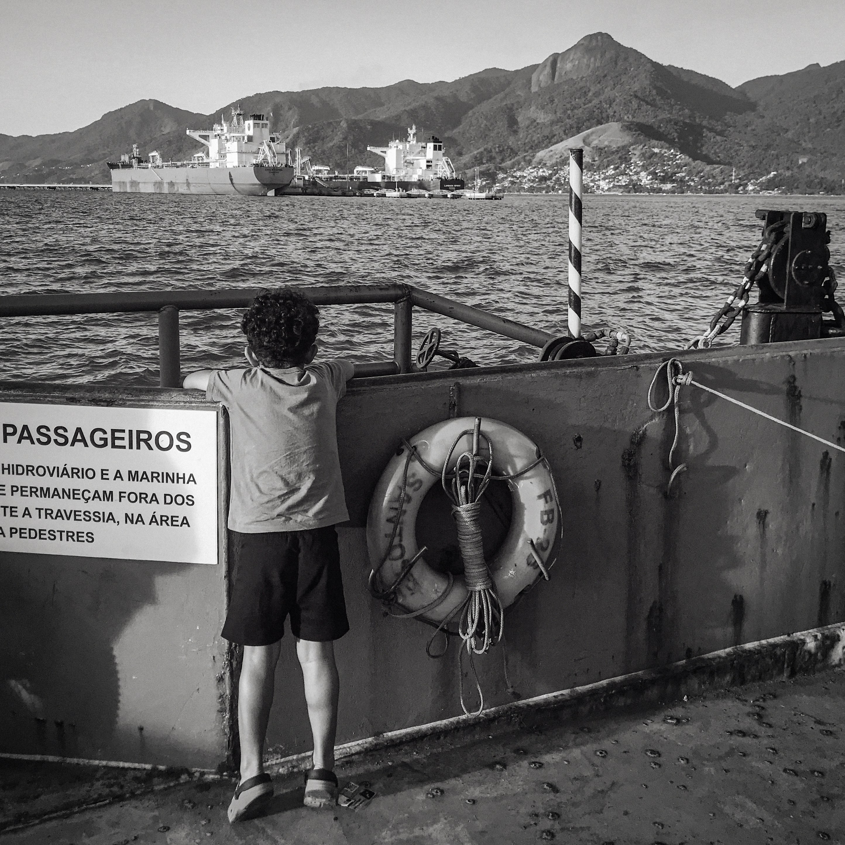 A boy watches ships in the harbor.