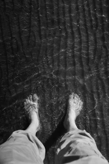 Feet stand in shallow water at the beach.