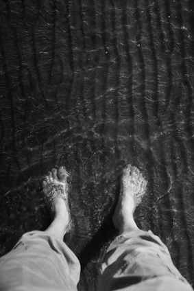 Feet stand in shallow water at the beach.
