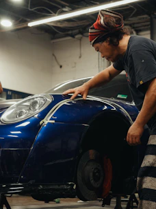 A mechanic works on a blue sports car.