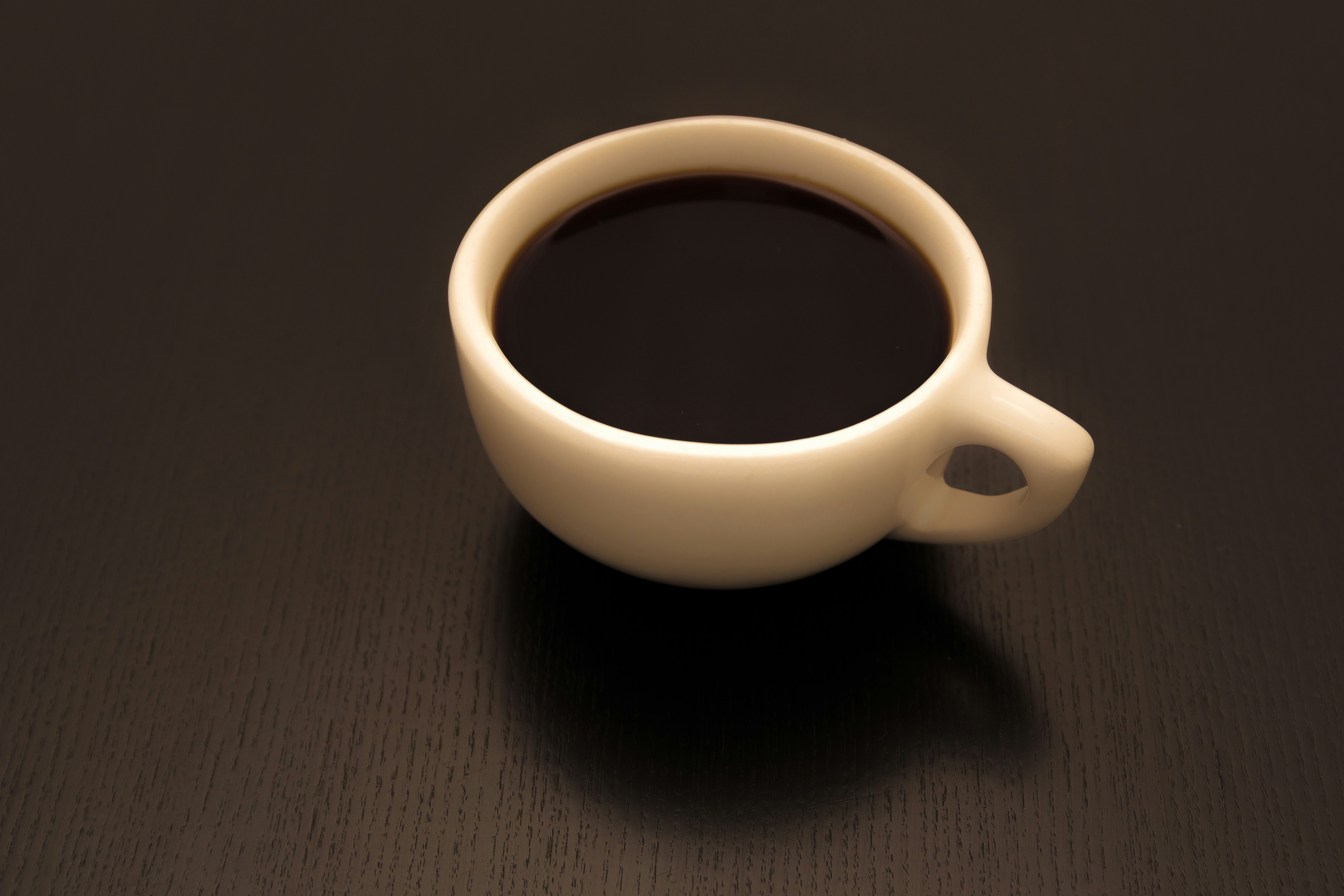 A cup of coffee is on a dark surface.
