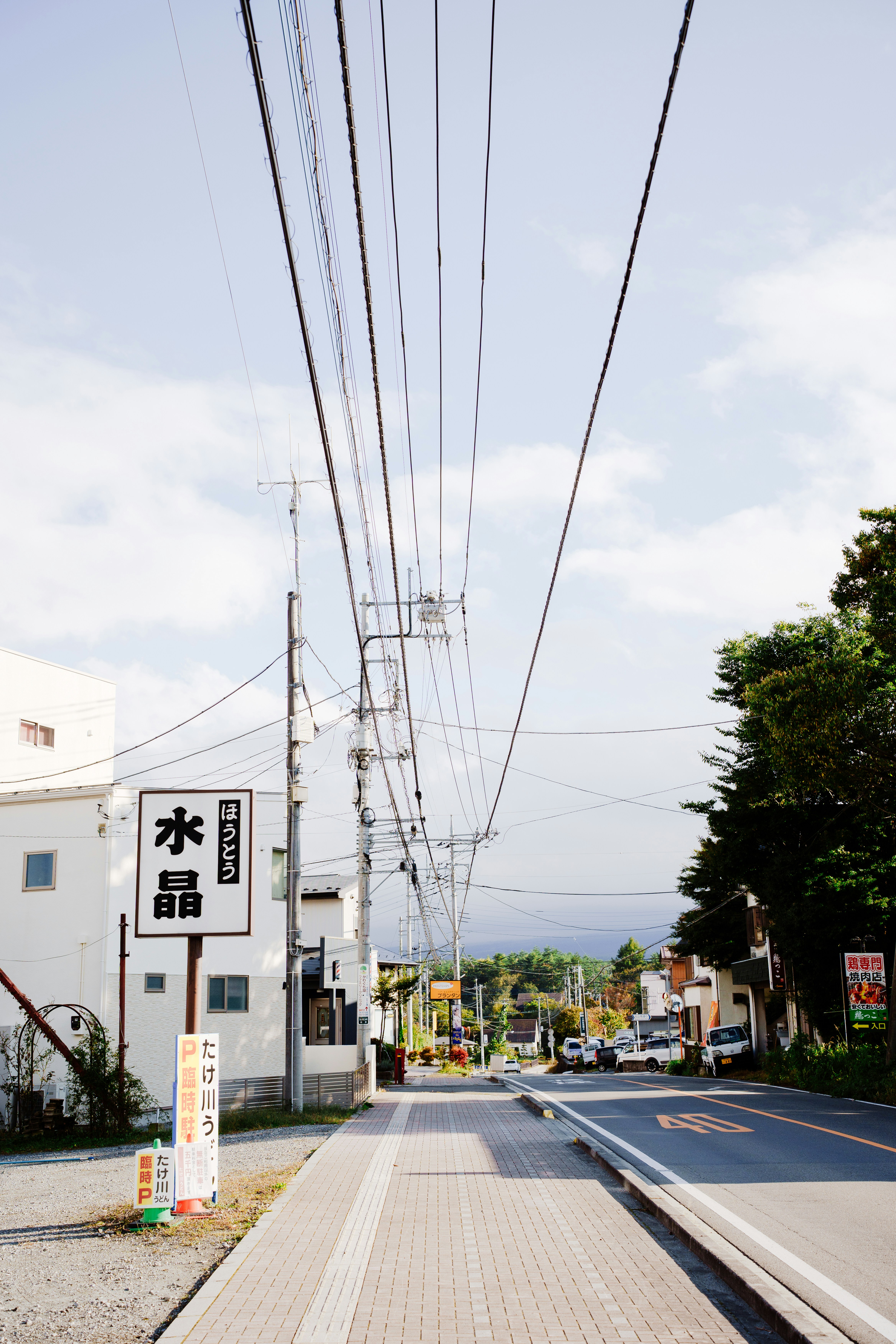 Road with power lines and buildings under a bright sky.