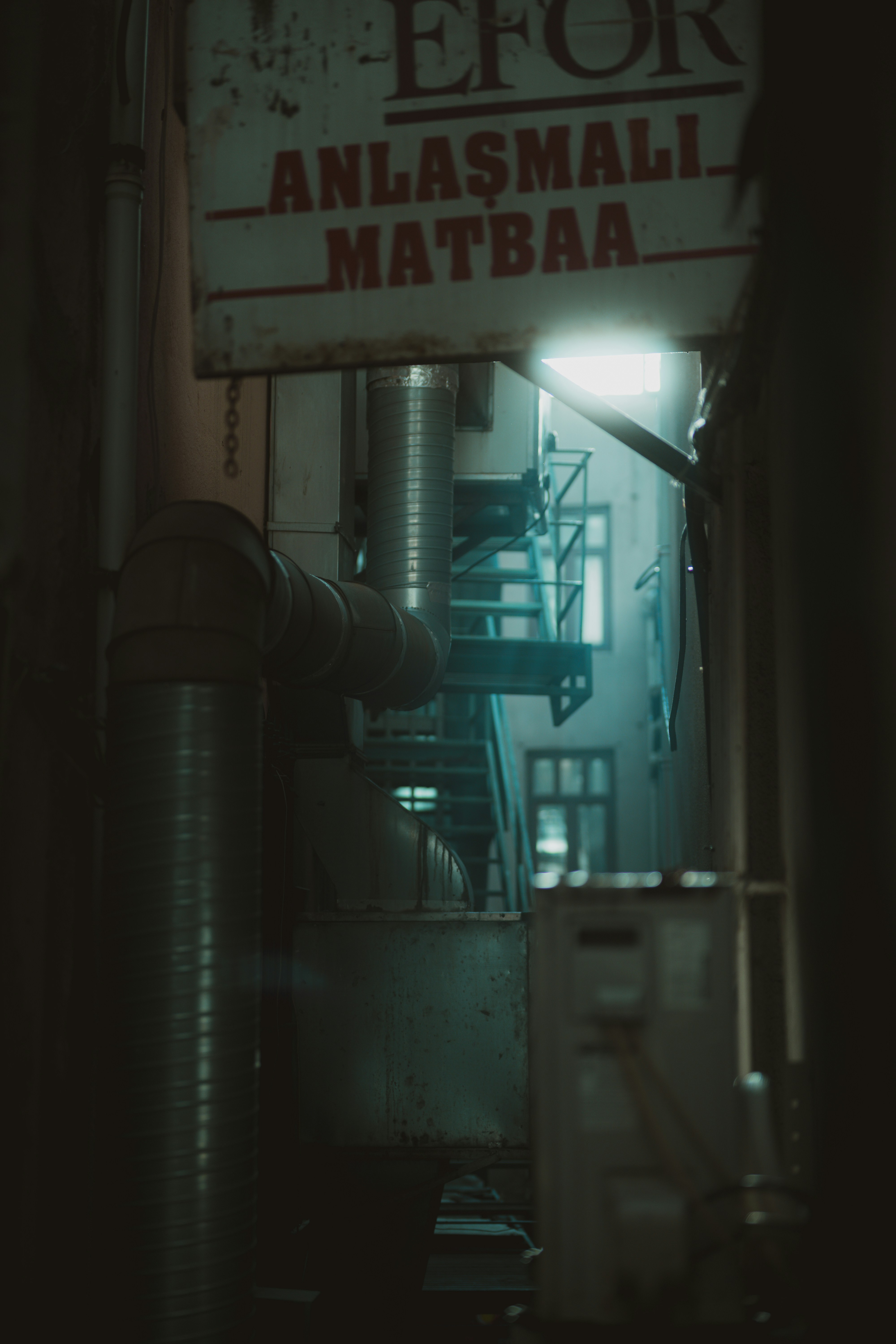 Dark alleyway with pipes and a sign.