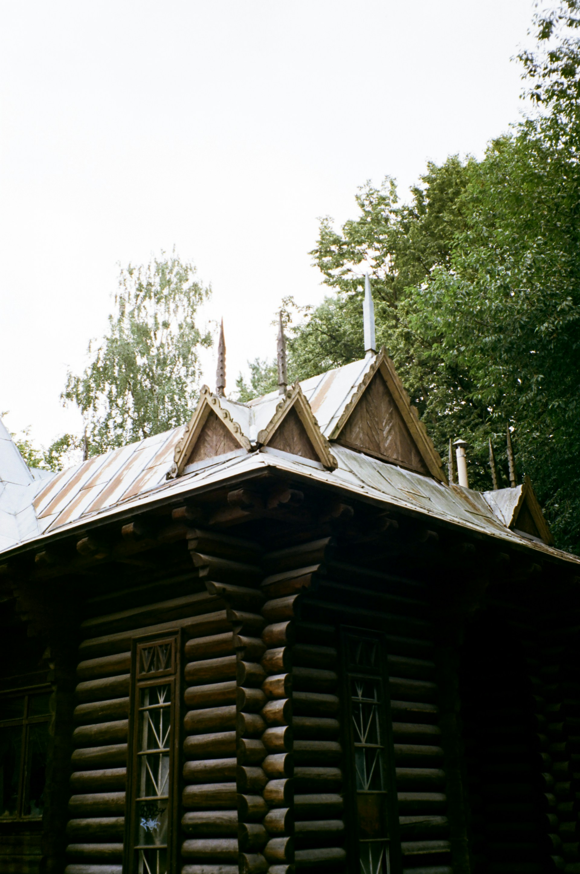 A wooden cabin sits beneath green trees.