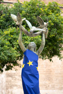 Statue of a woman holding doves, draped in the eu flag.