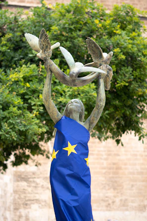 Statue of a woman holding doves, draped in the eu flag.