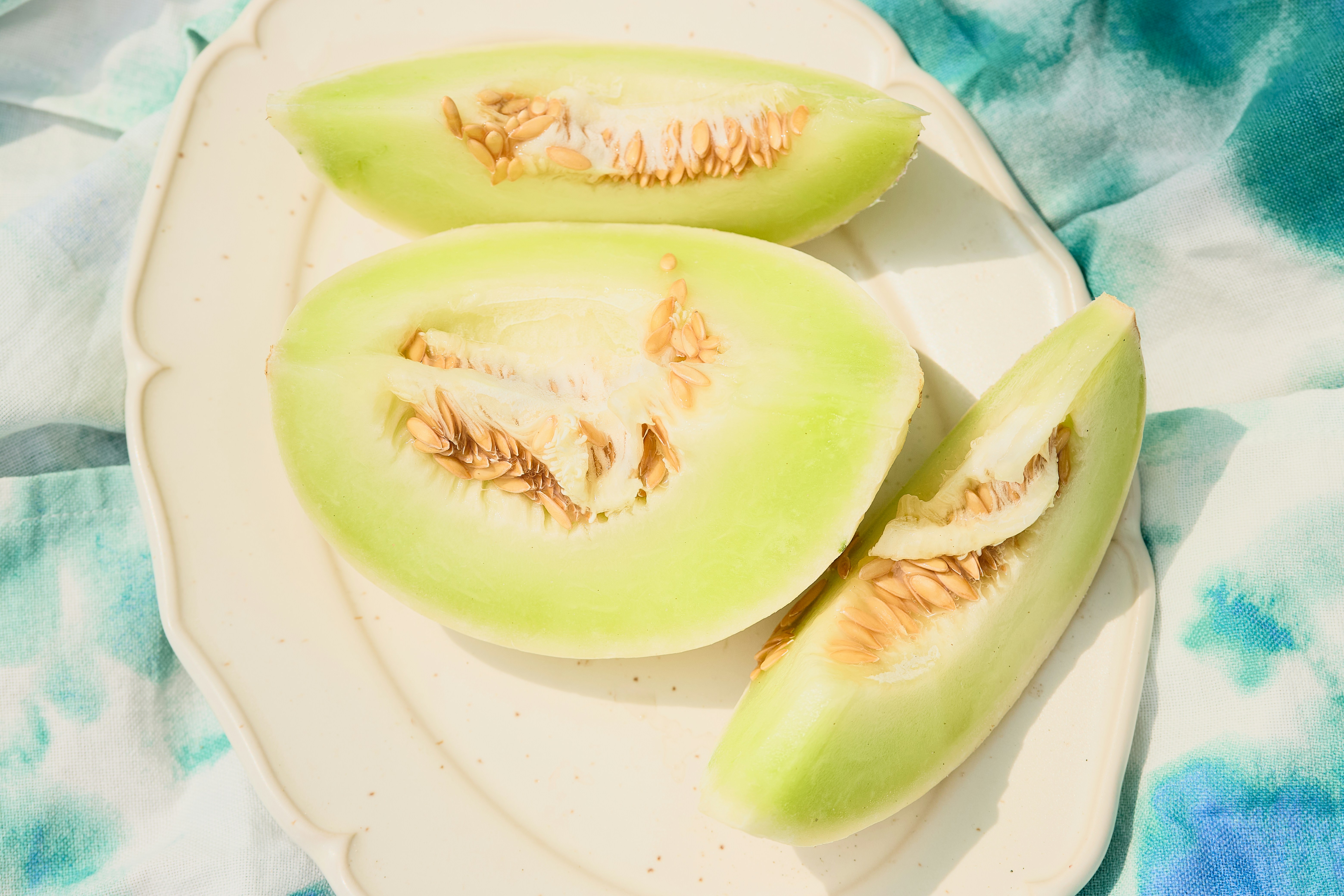 Cantaloupe melon slices sit on a white plate.