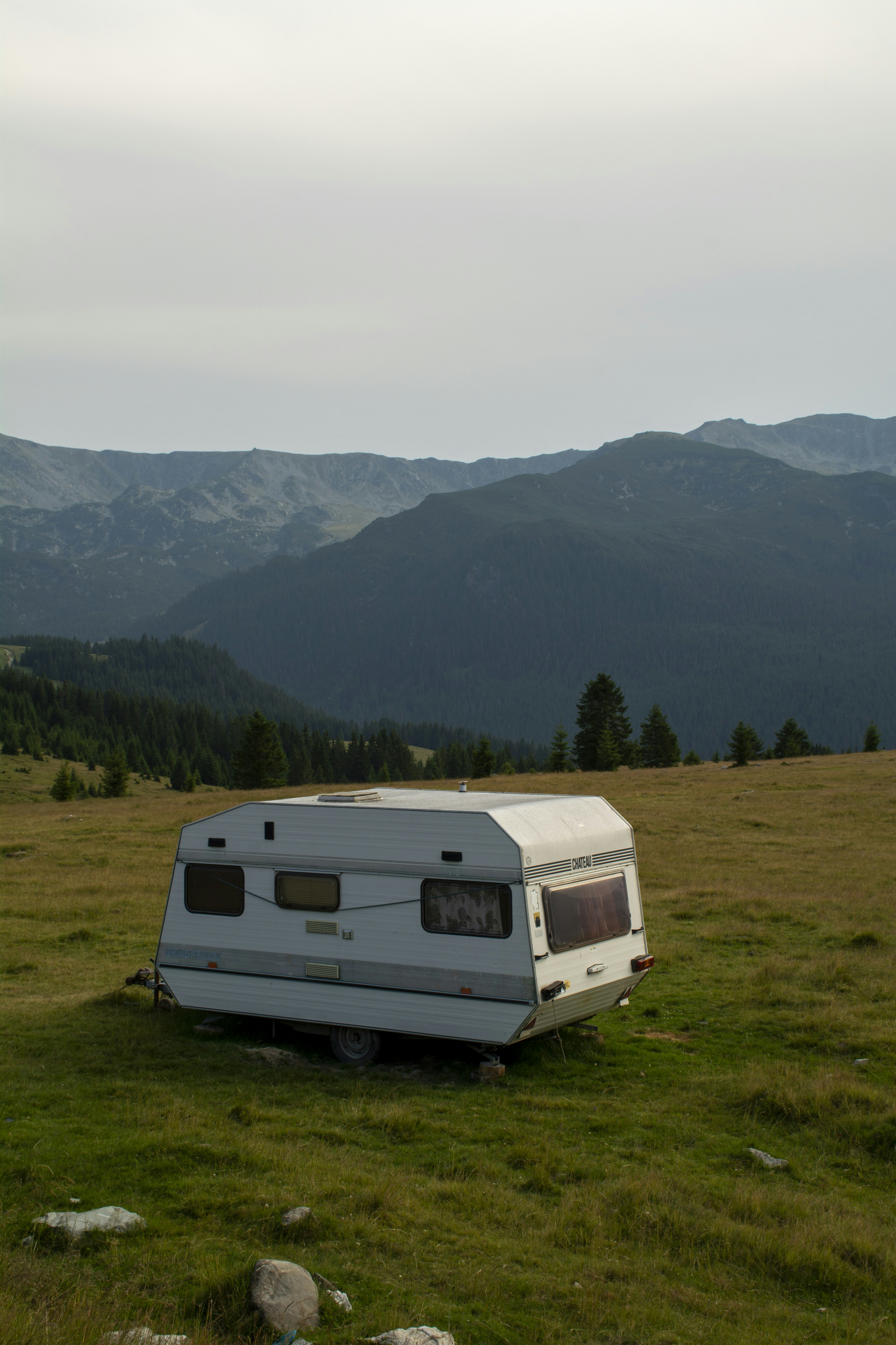A camper sits on a grassy field near mountains.