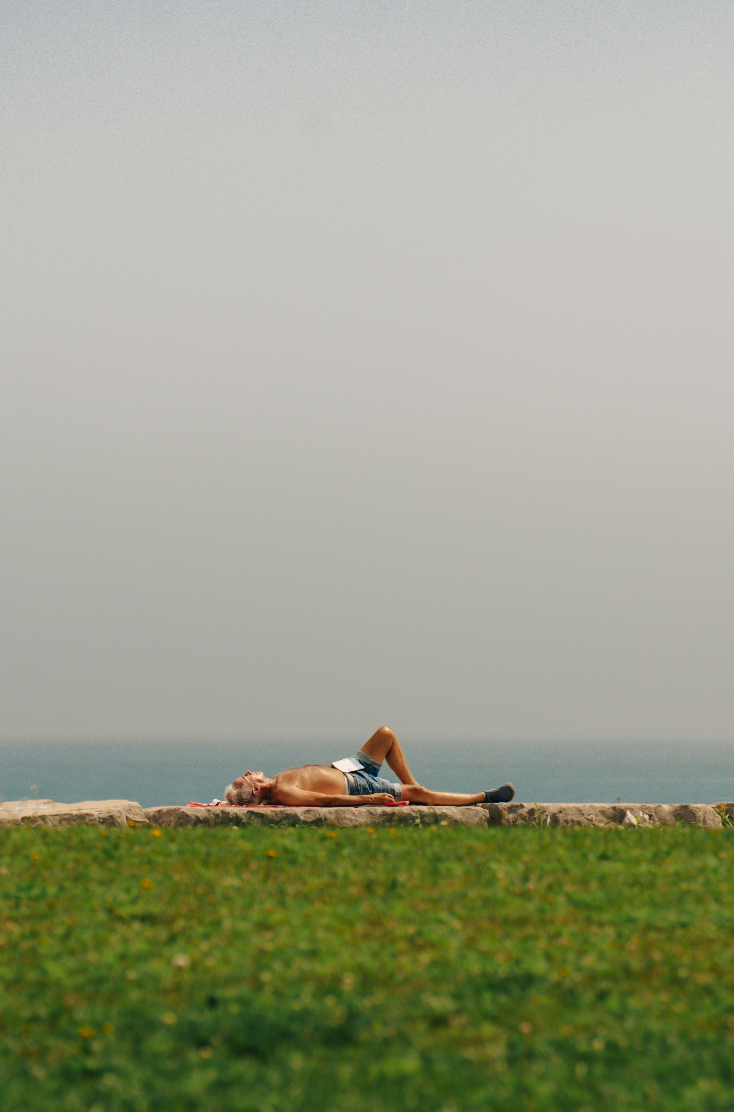 Man relaxes and sunbathes on a grassy ledge.