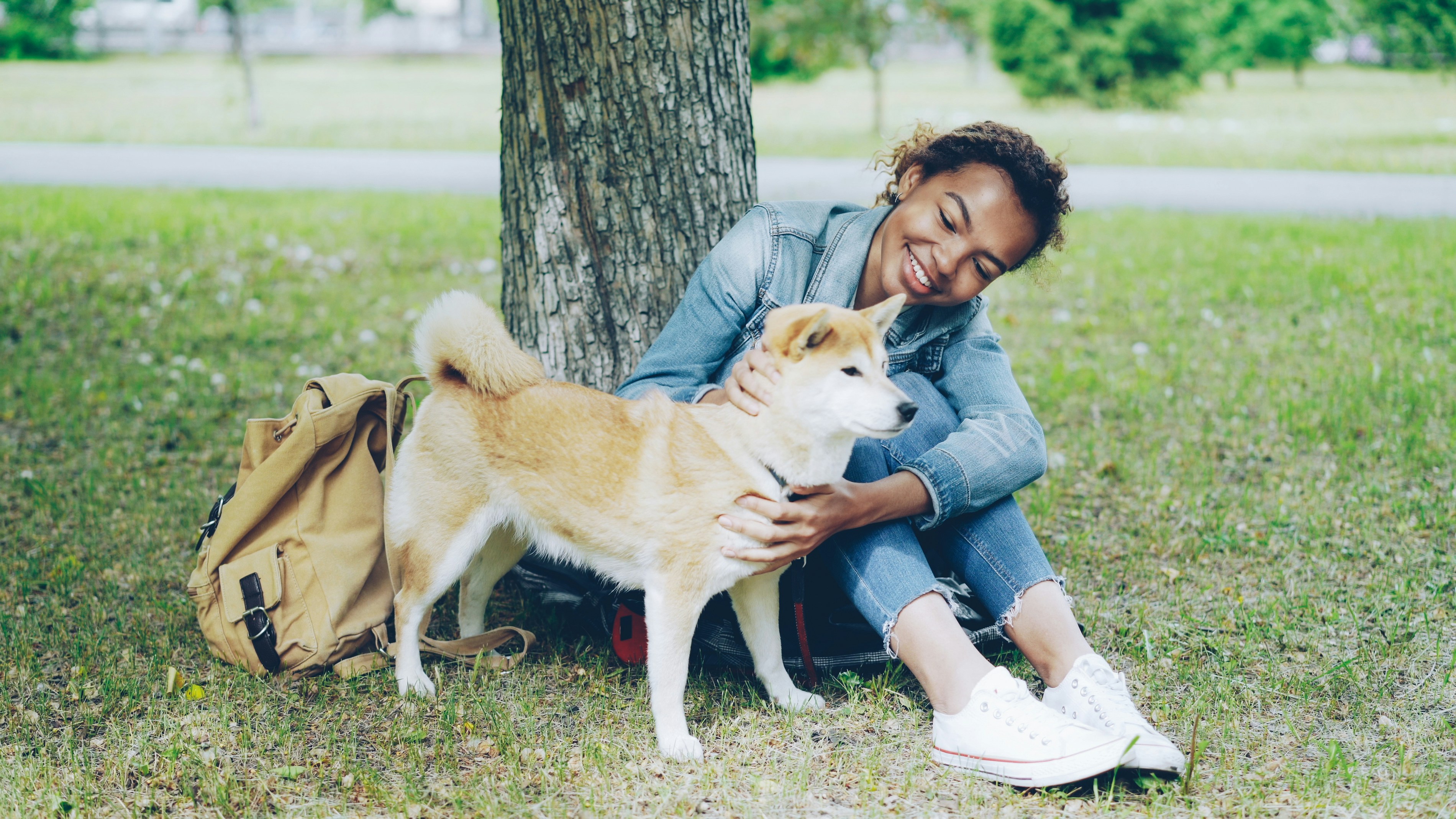 Woman smiles while petting her dog in a park.