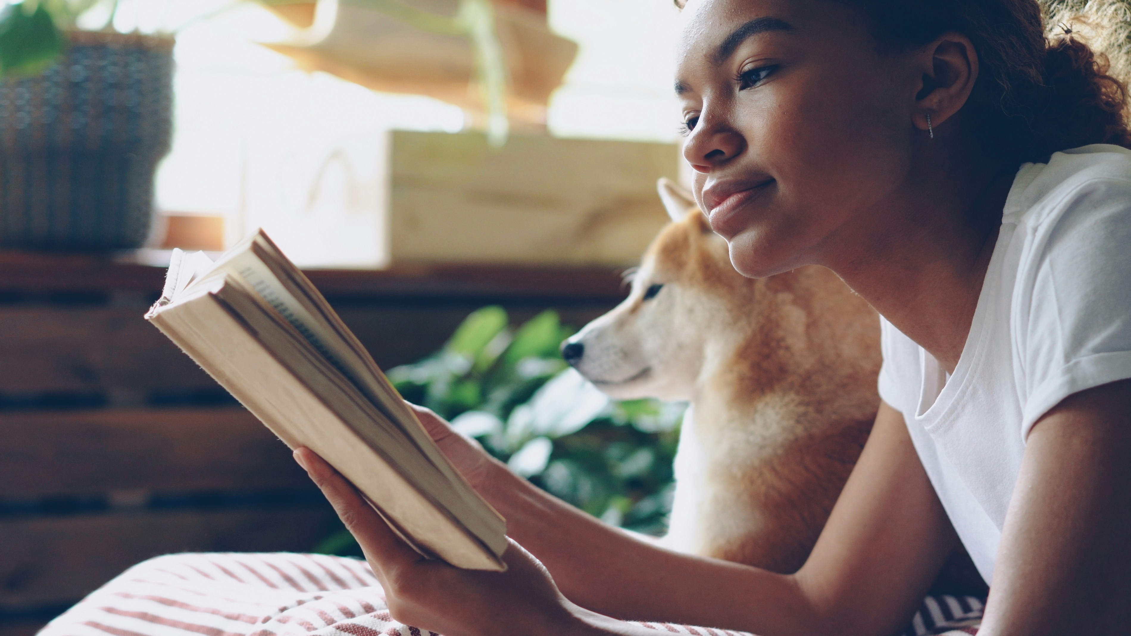 Girl reads a book with her dog nearby.