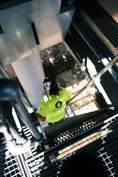 A worker in a green shirt climbs stairs.