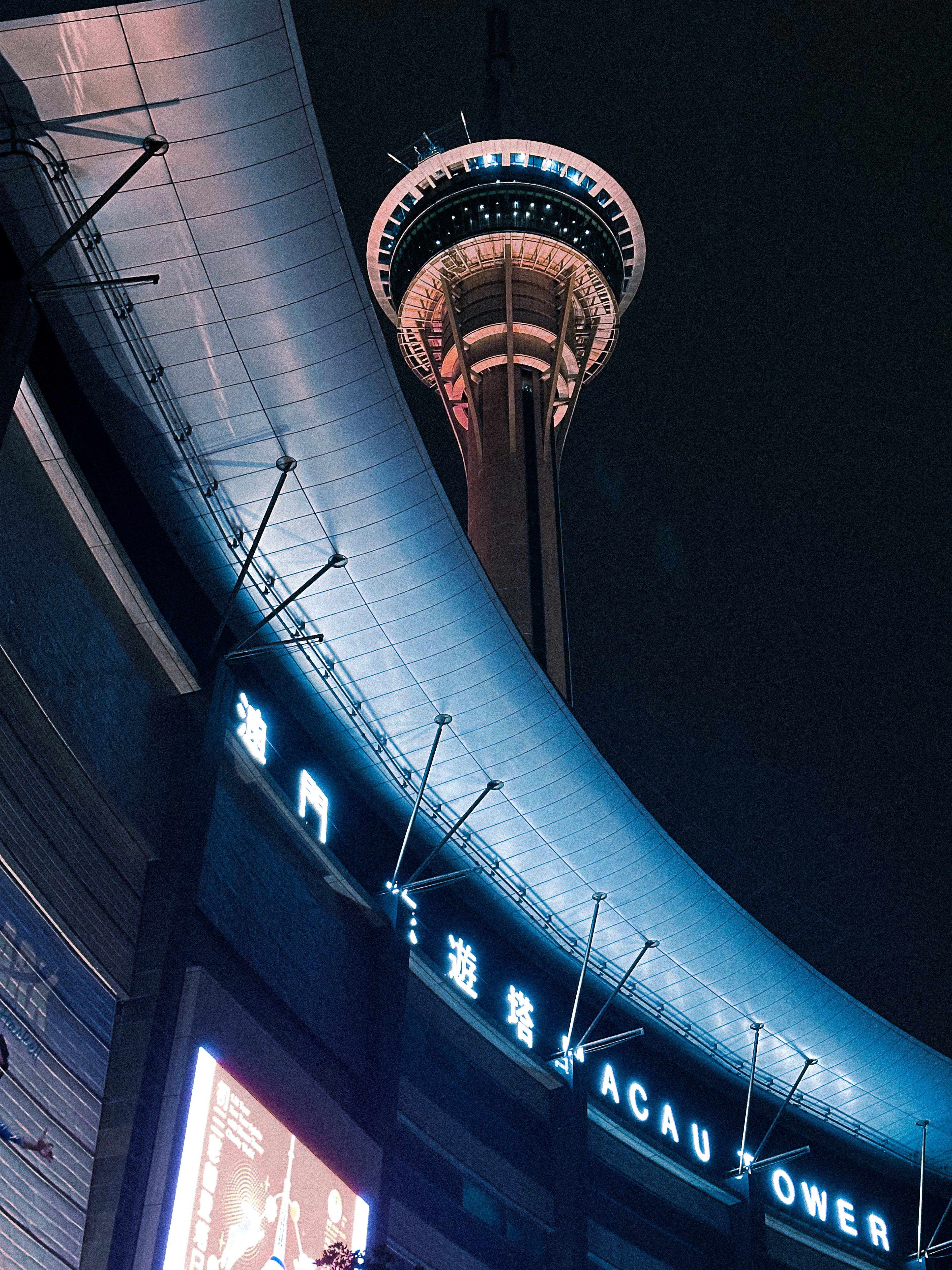 Macau Tower glowing blue at night beneath the curved underside of its observation deck.
