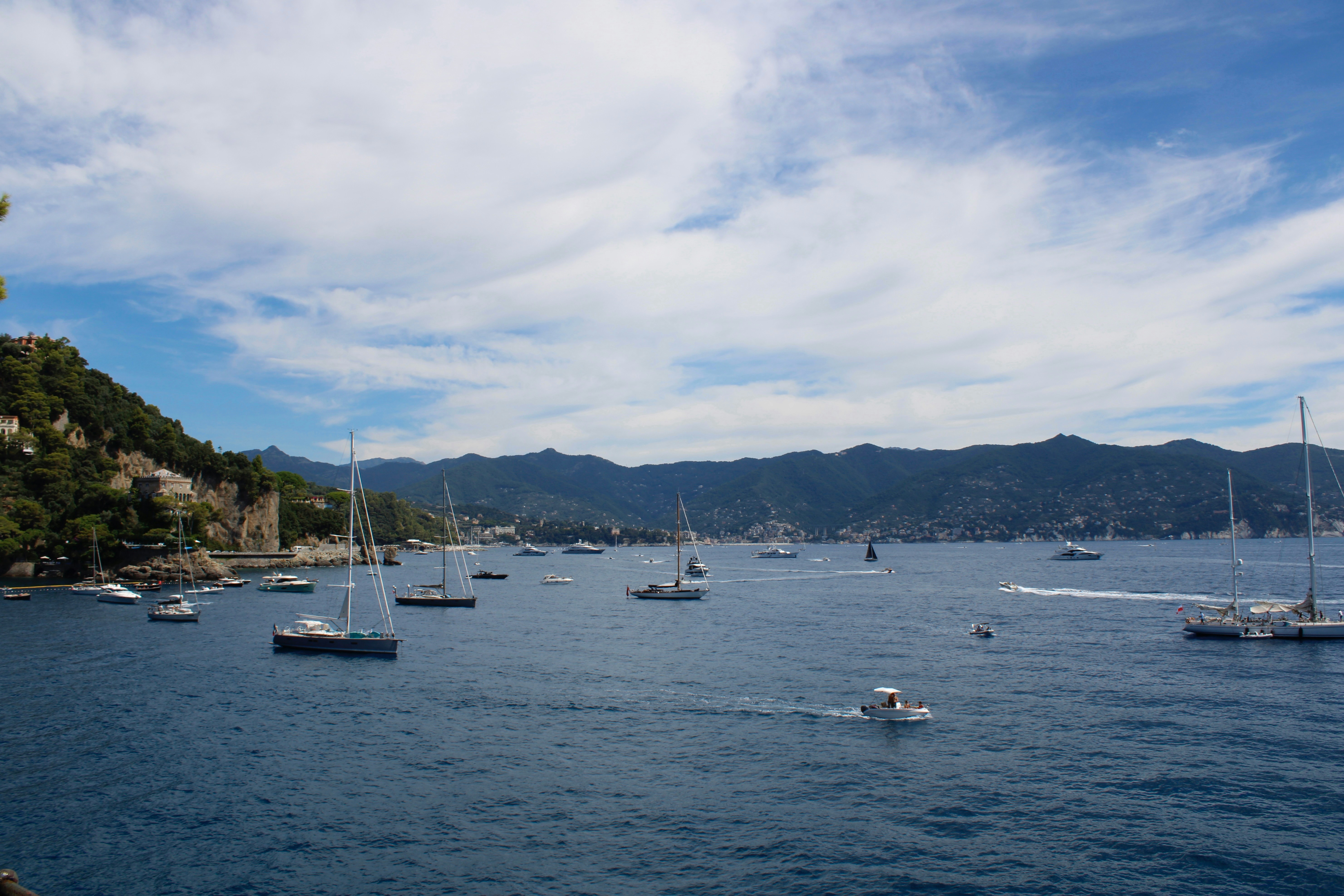 Sailboats dot the blue sea under a cloudy sky.