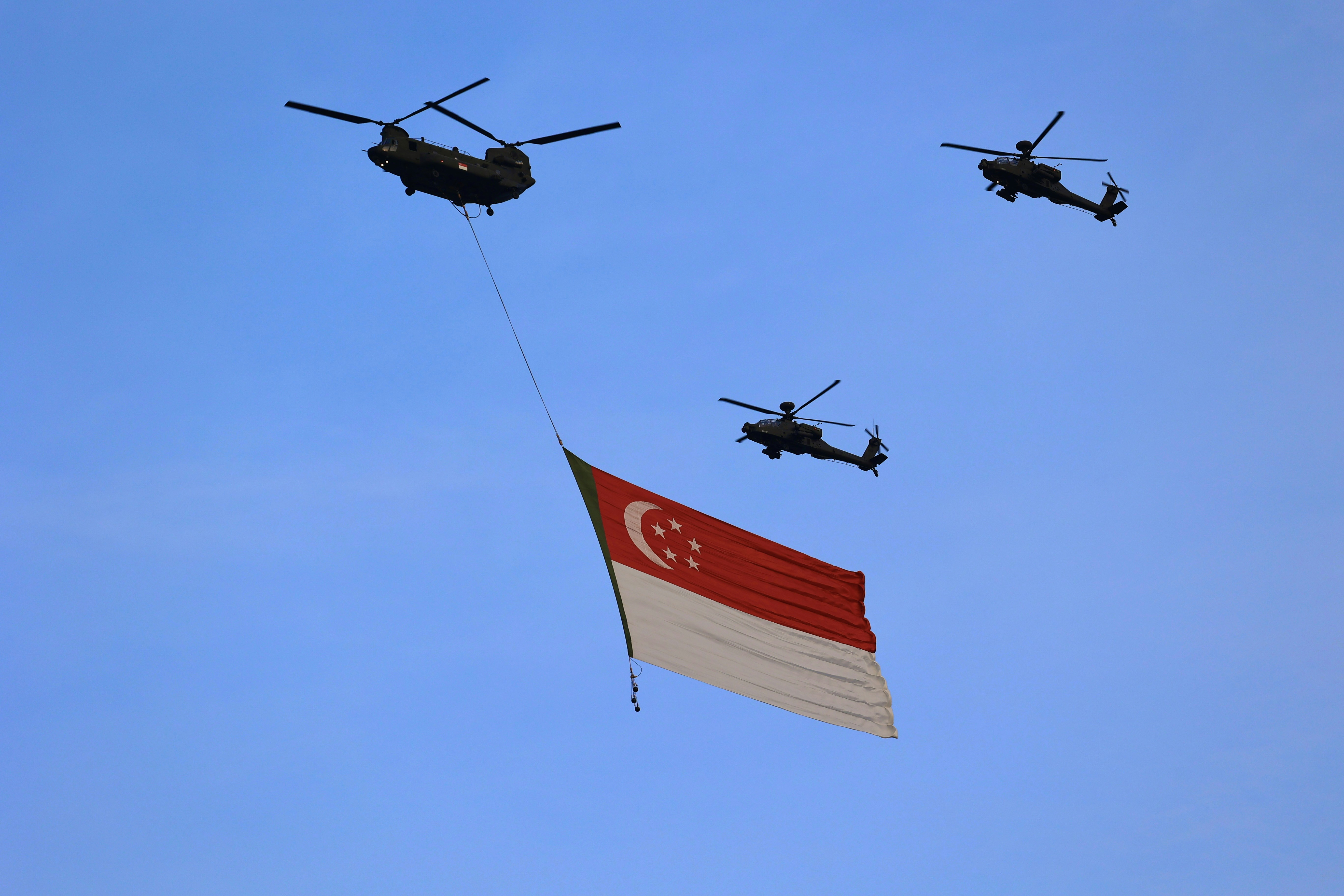 Helicopters fly with the singapore flag.