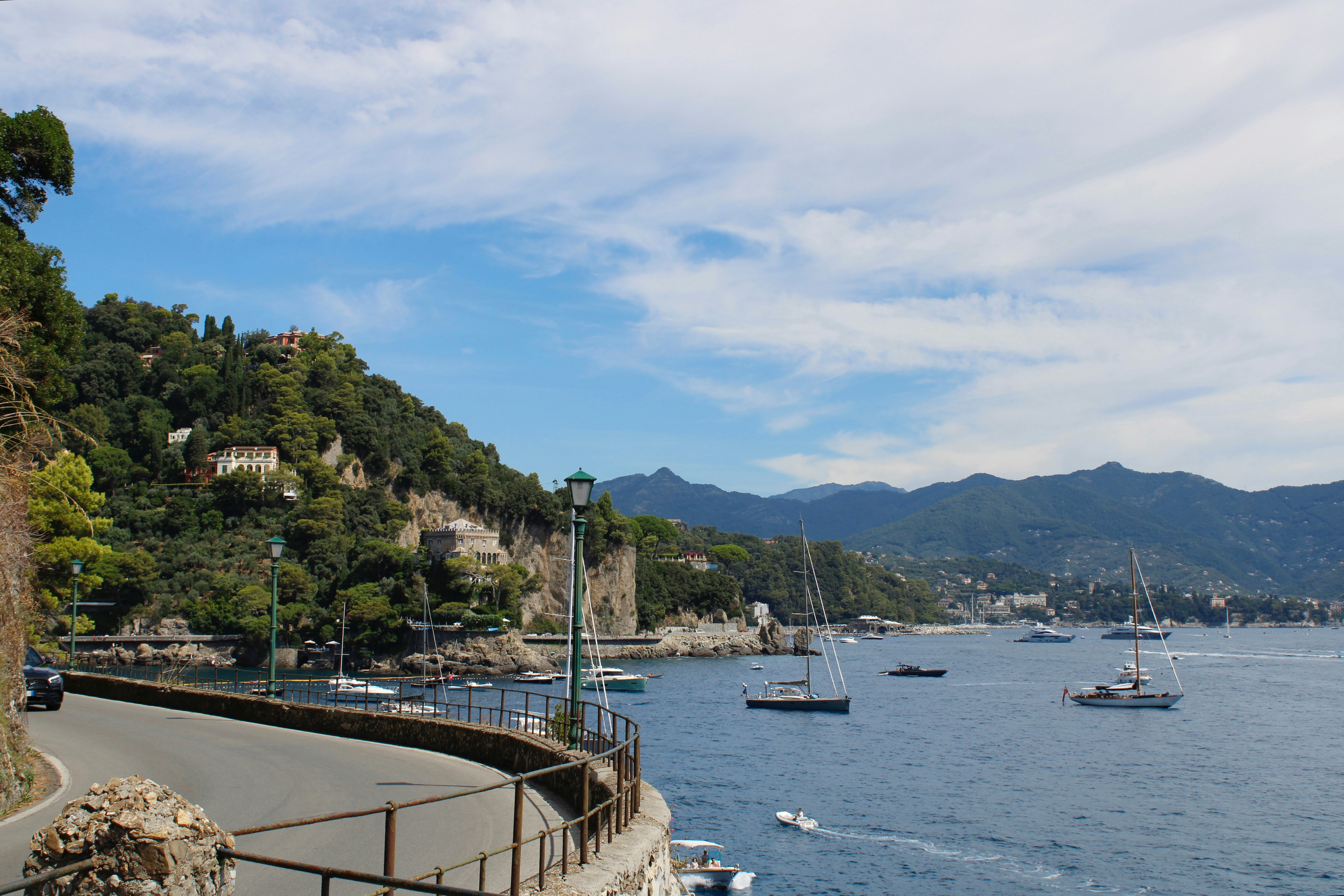 Coastal road with boats sailing on the water.