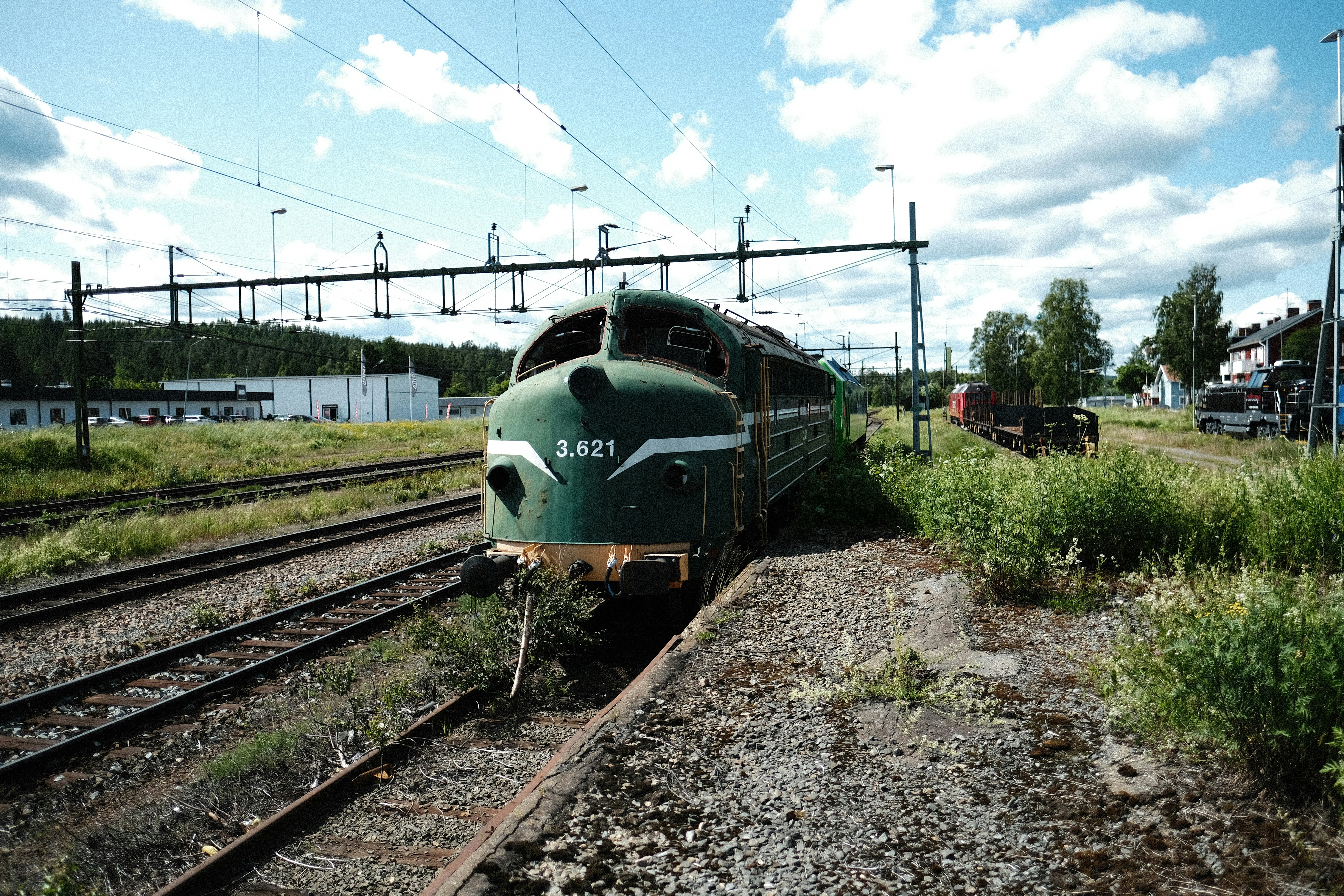 A green train waits on the tracks outdoors.