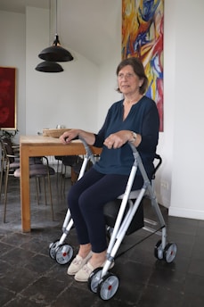 An elderly woman is seated on a walker.