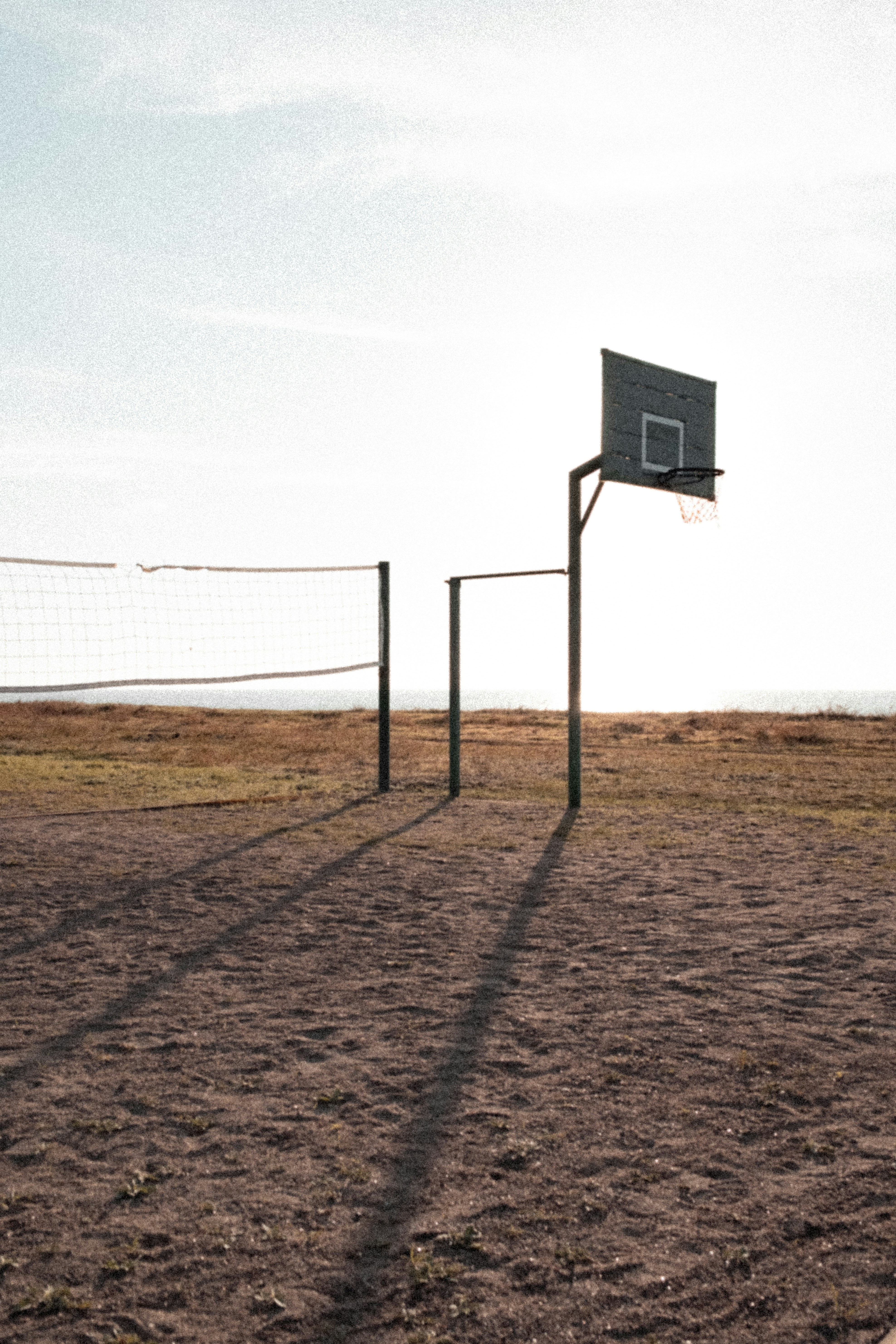 Aro de basquete e rede de vôlei em um campo arenoso.