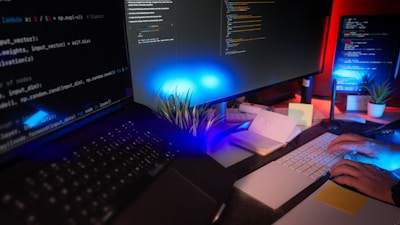 Un programmatore che digita a una scrivania con due monitor pieni di codice, illuminati da lampade colorate