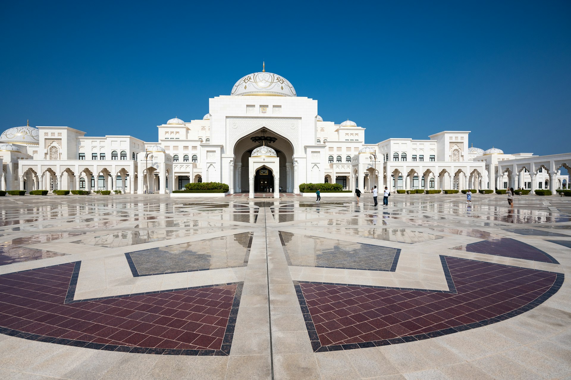 A large, white palace reflects on a fountain.