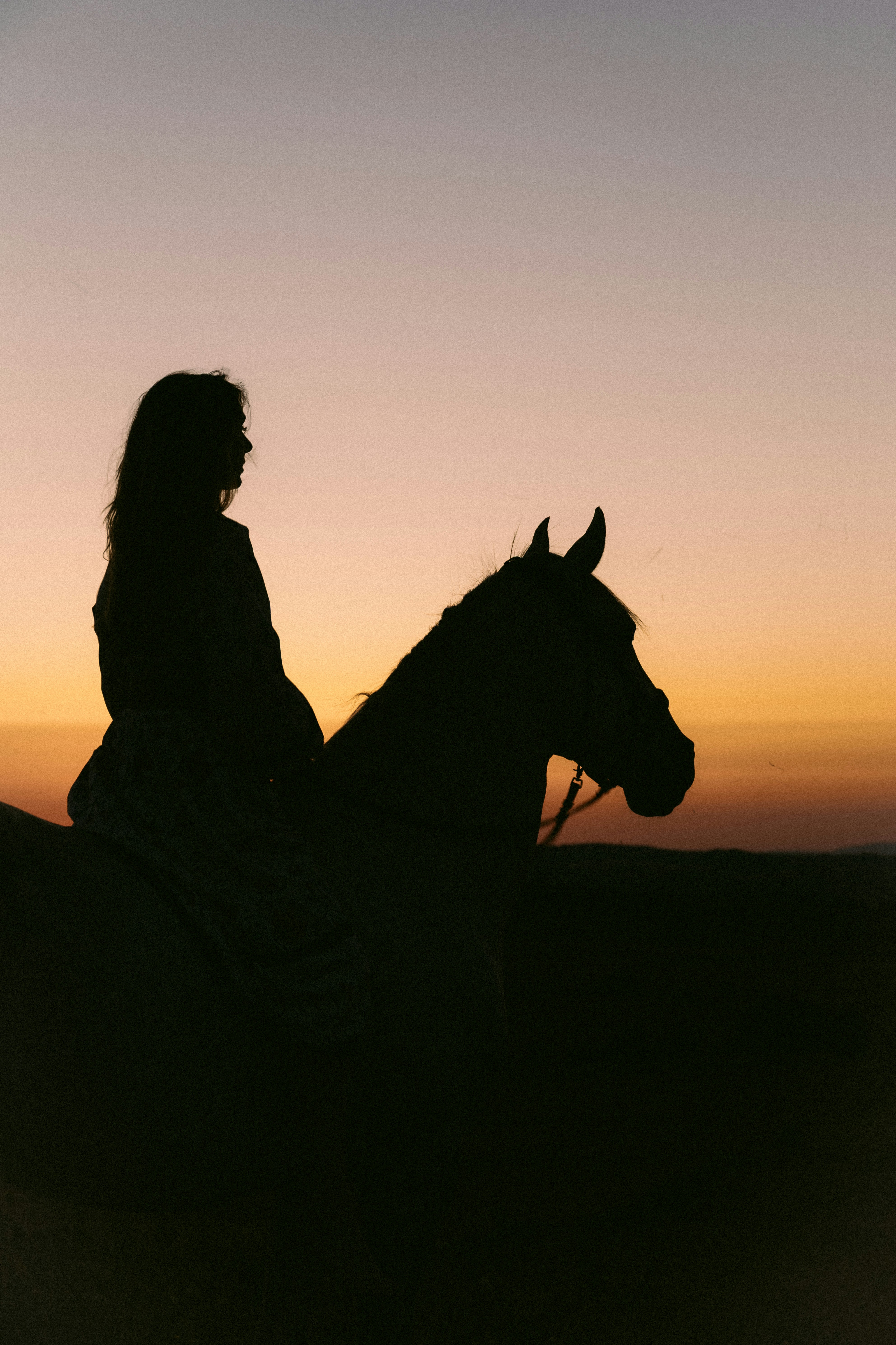 Silhouette of a woman riding a horse at sunset.