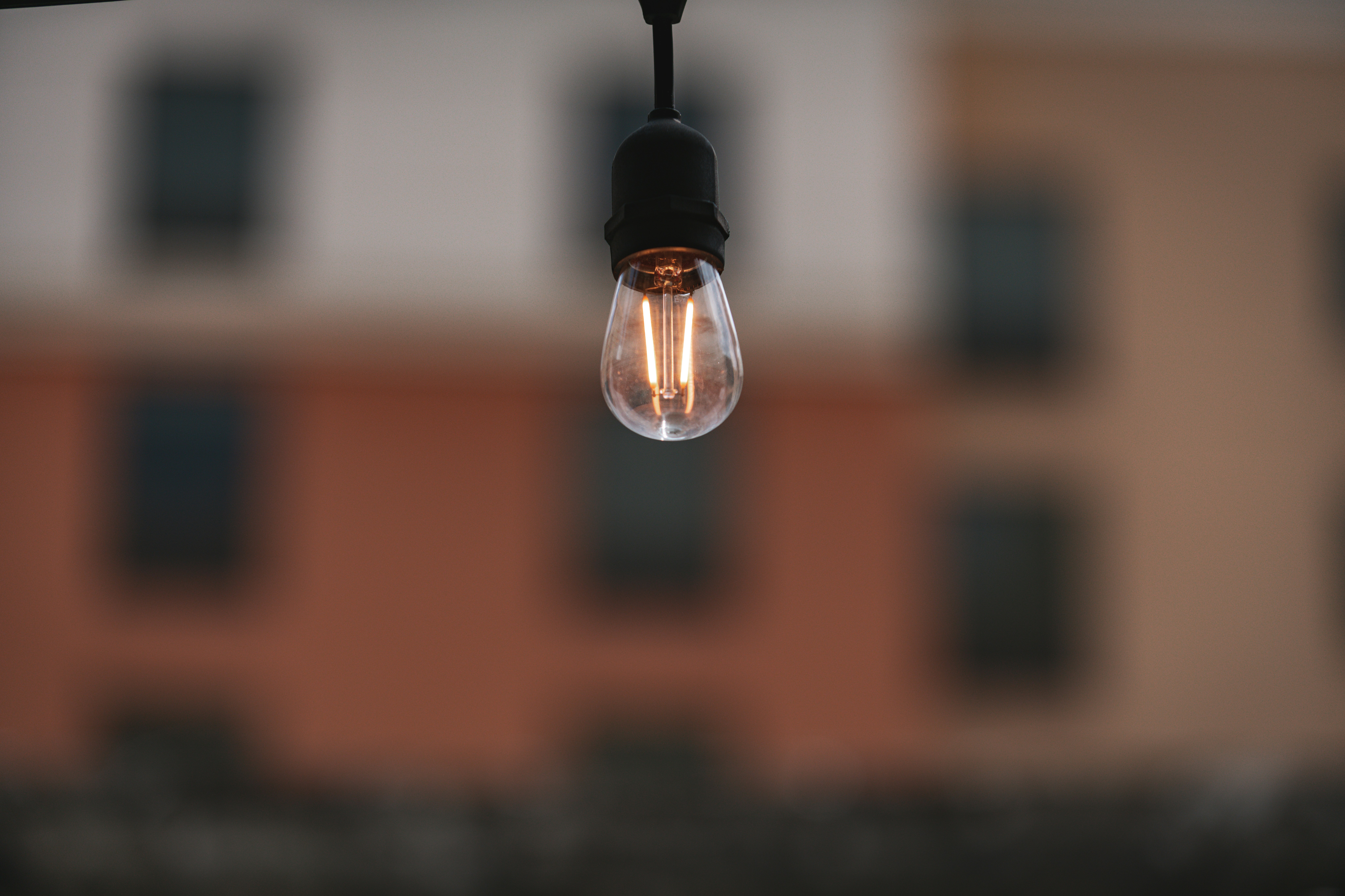 Lit lightbulb dangles against blurred building.