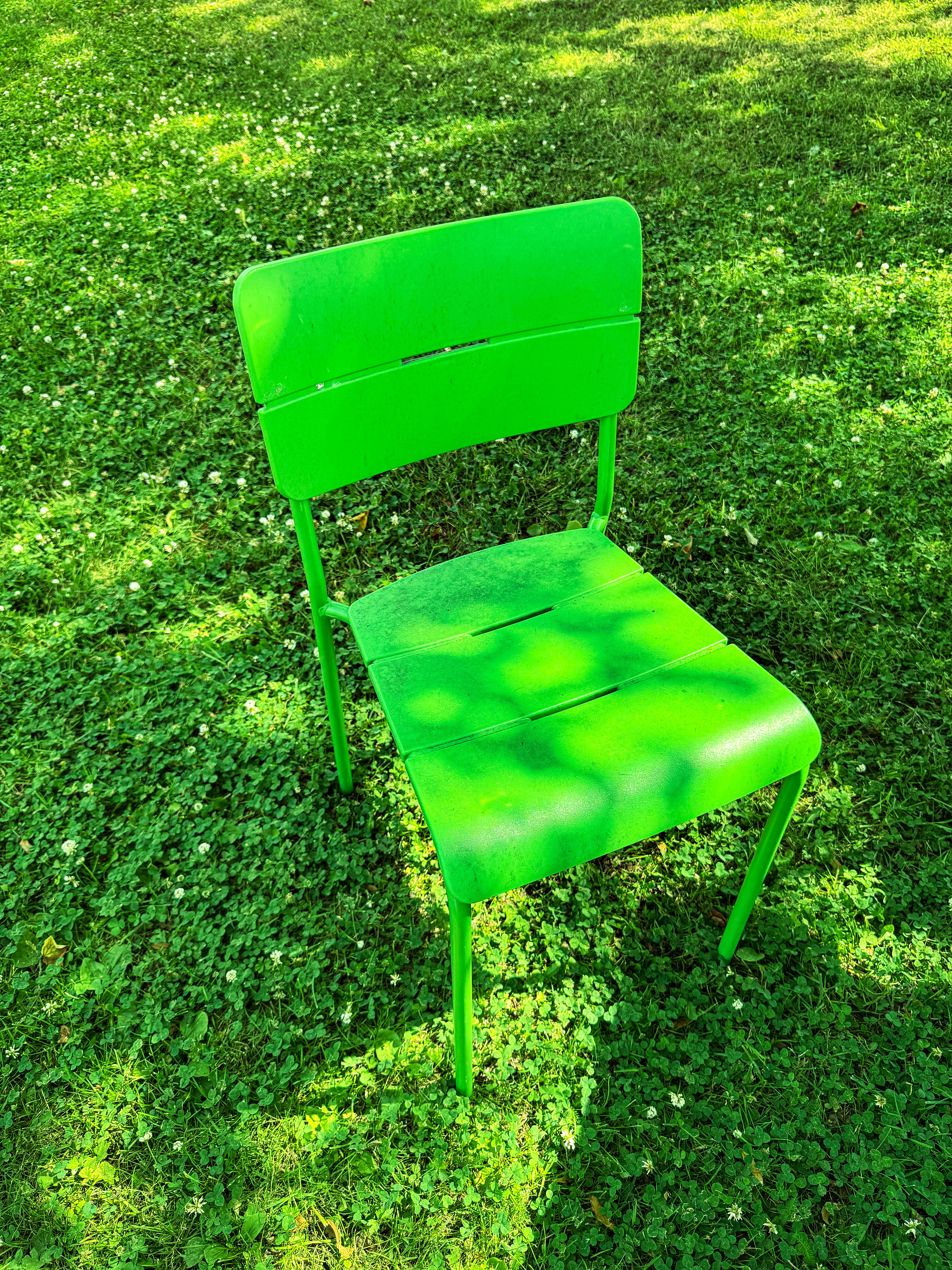 A green chair sits on a lush green lawn.