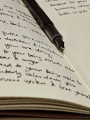 A fountain pen rests atop handwritten journal entries.