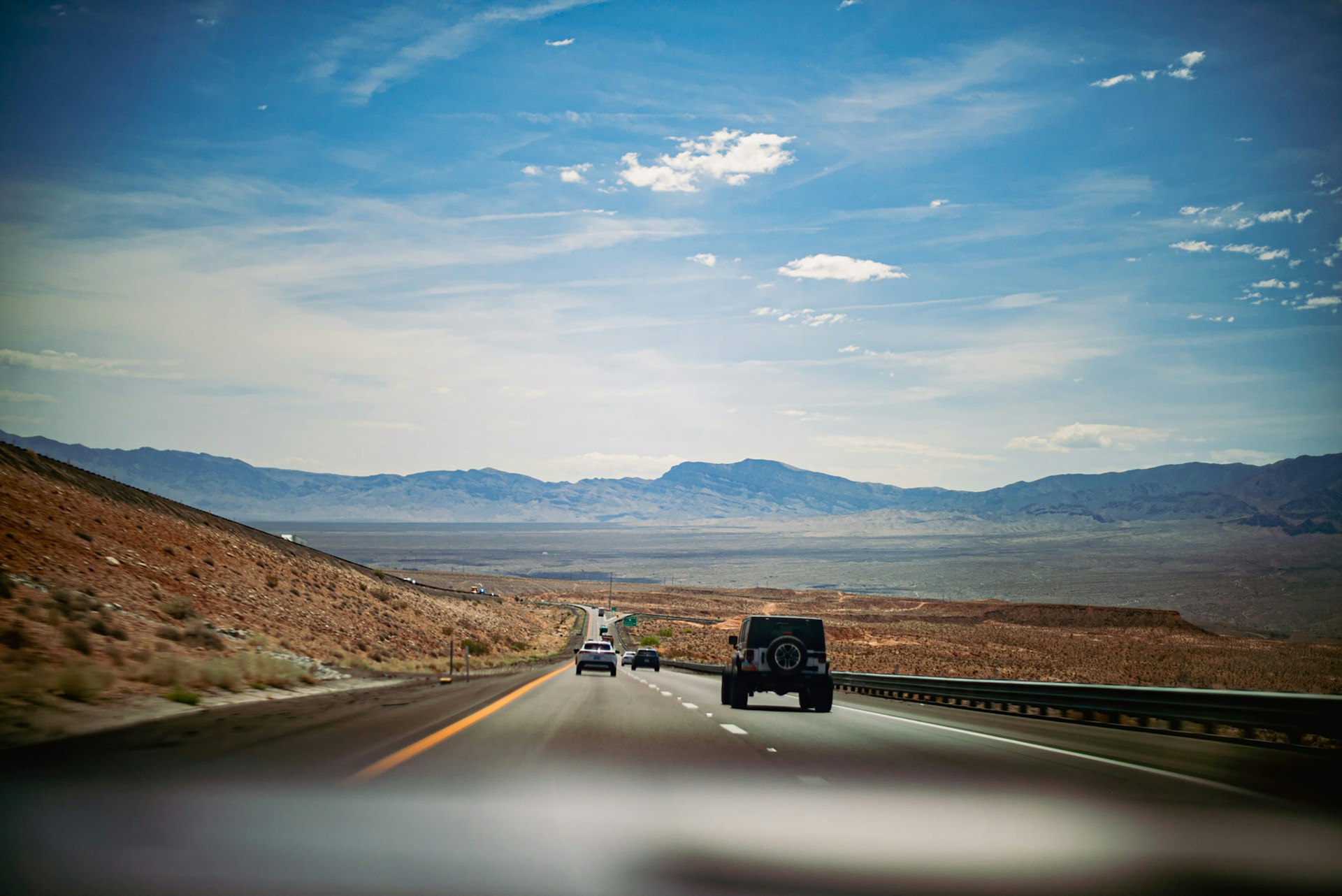 Cars drive down a desert highway towards mountains.