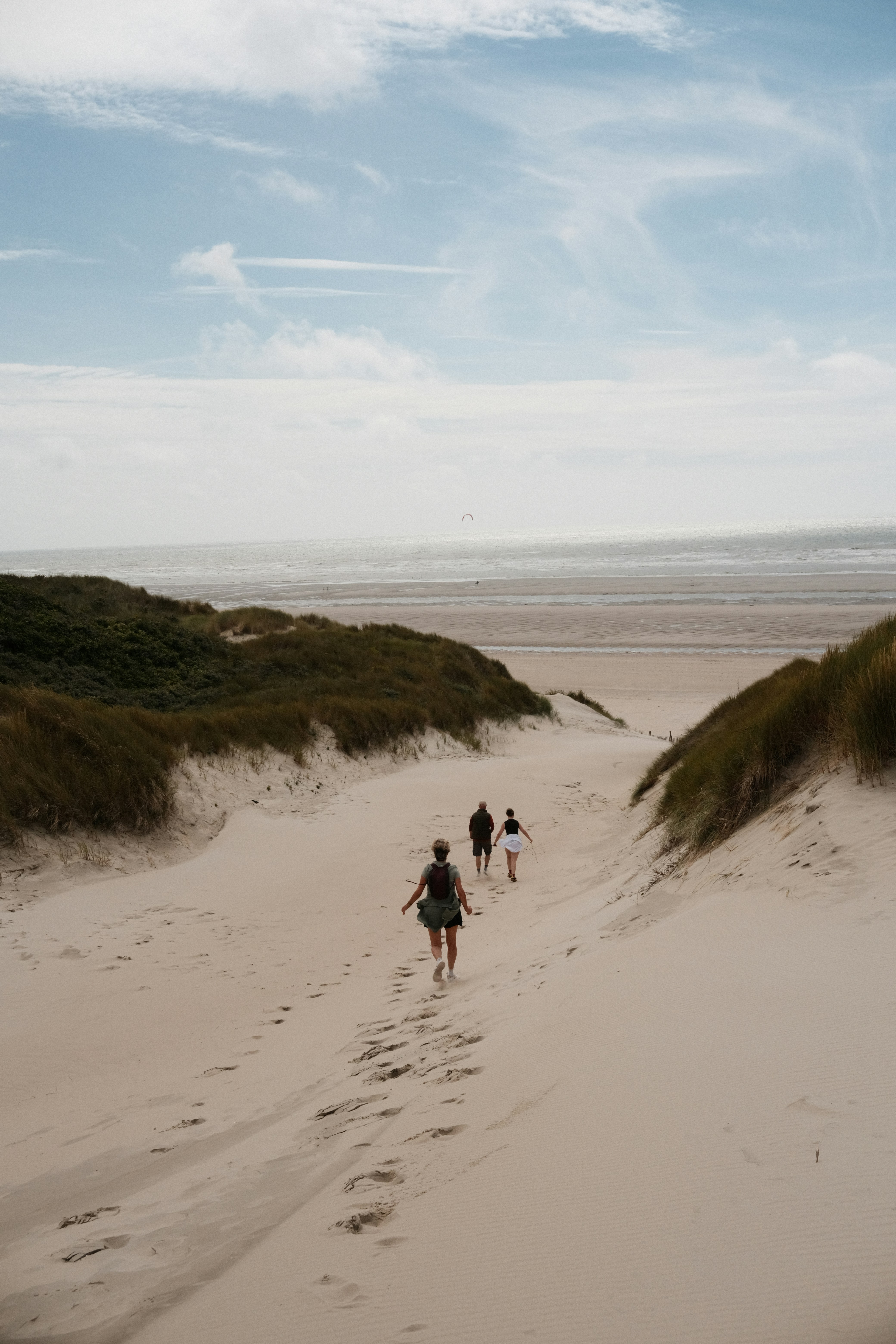 People hike through sand dunes towards the ocean.