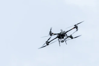 A drone flies against a cloudy sky.