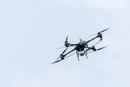 A drone flies against a cloudy sky.