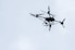 A drone flies high against a cloudy sky.