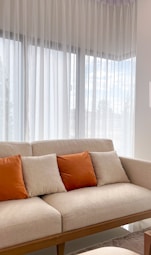 A couch with orange pillows sits by a window.