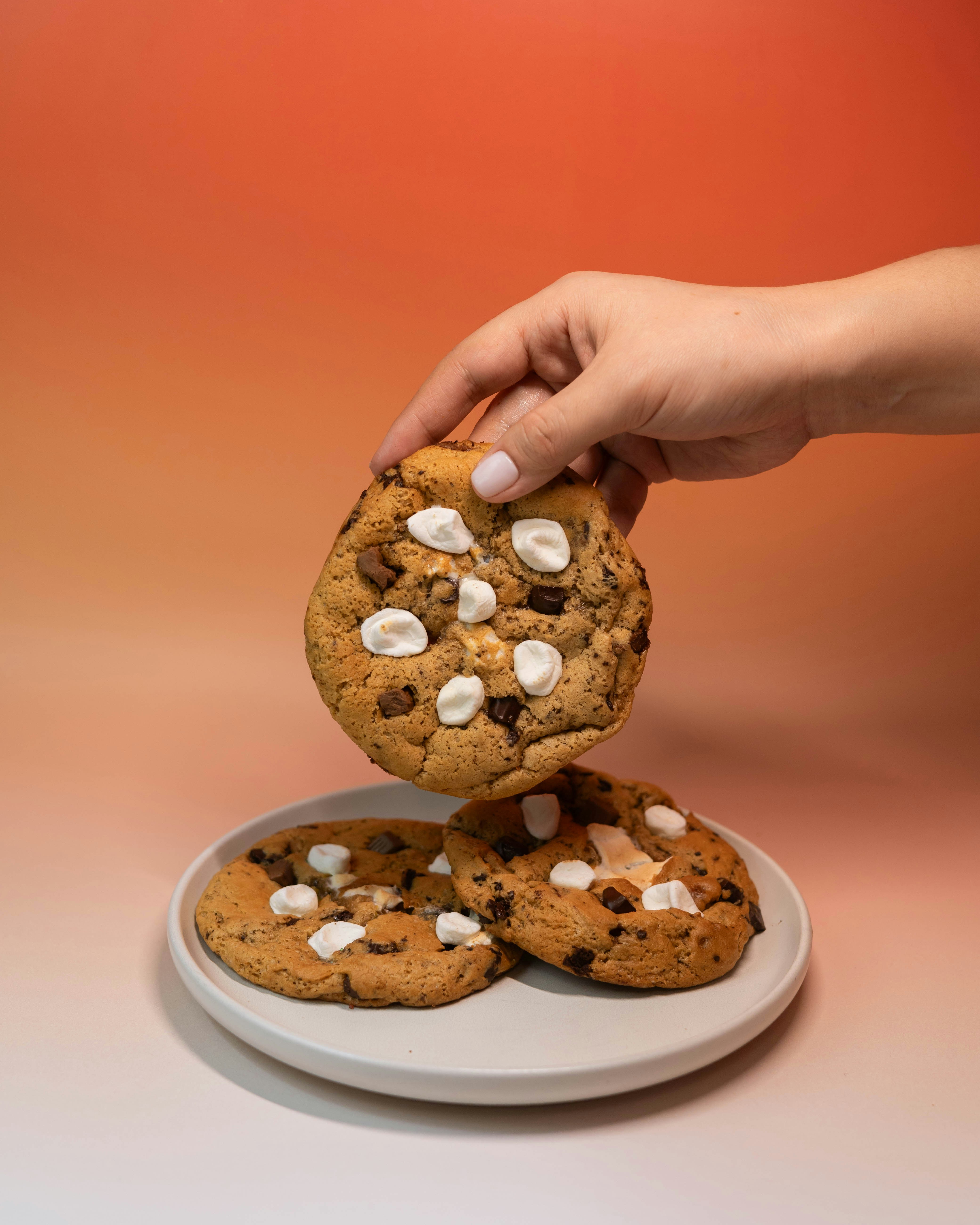Hand lifting cookie from plate of cookies.
