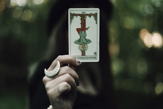 A hand holds the hanged man tarot card.