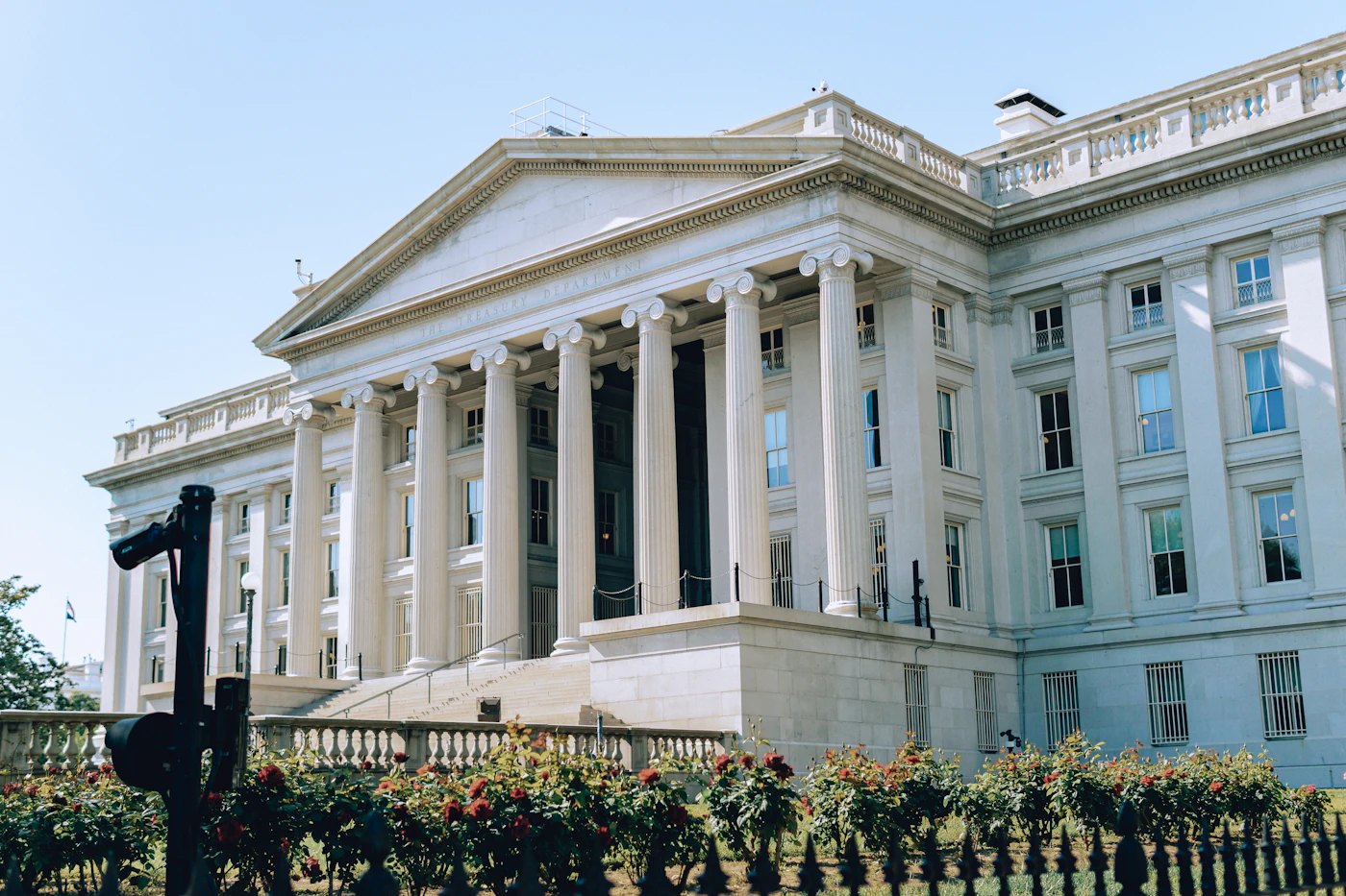 Columned facade of the US Treasury Building in Washington on a sunny day, behind a flower bed