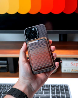 A hand holds a phone with wallet case attached.