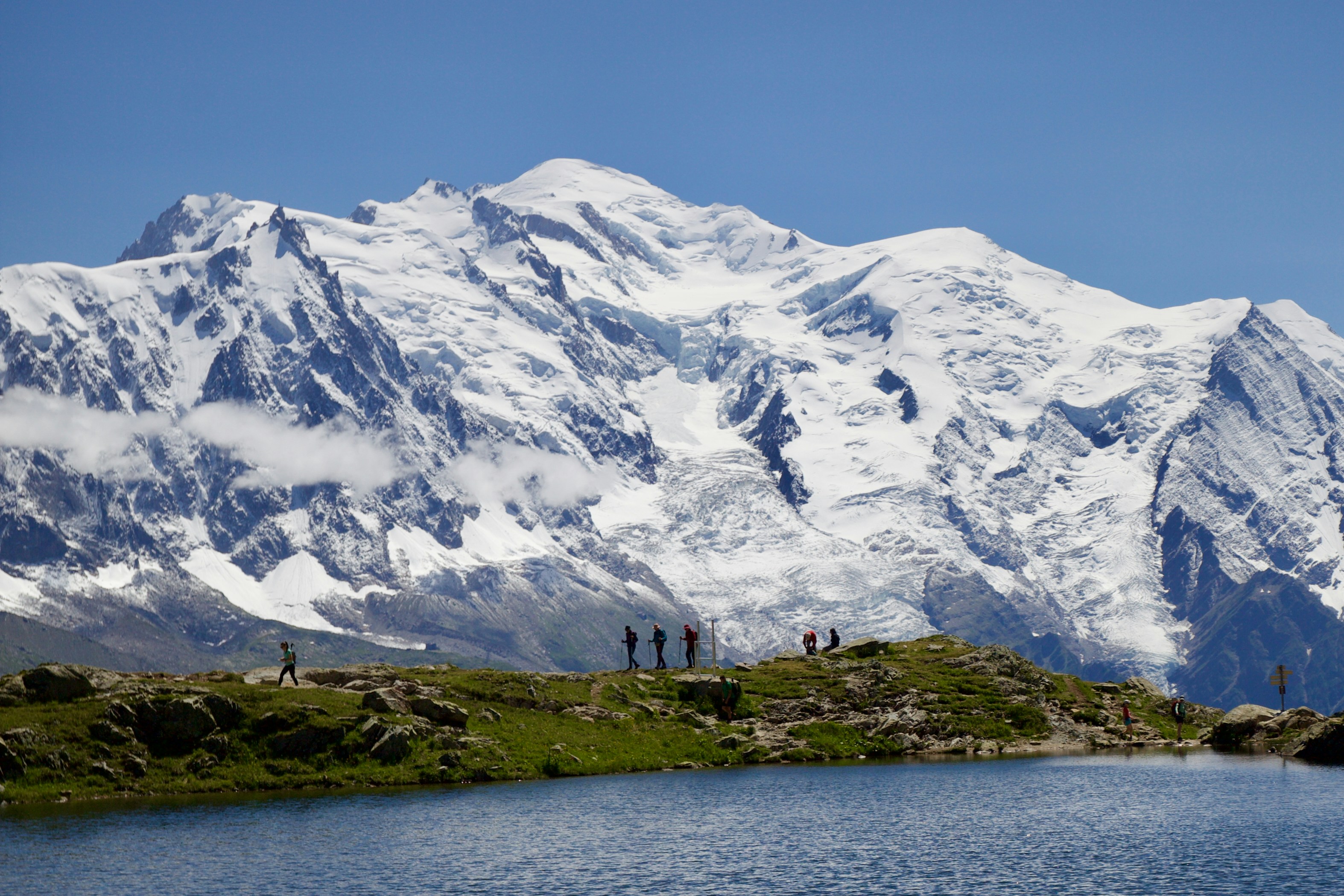Snow-capped mountains tower over a still, blue lake.