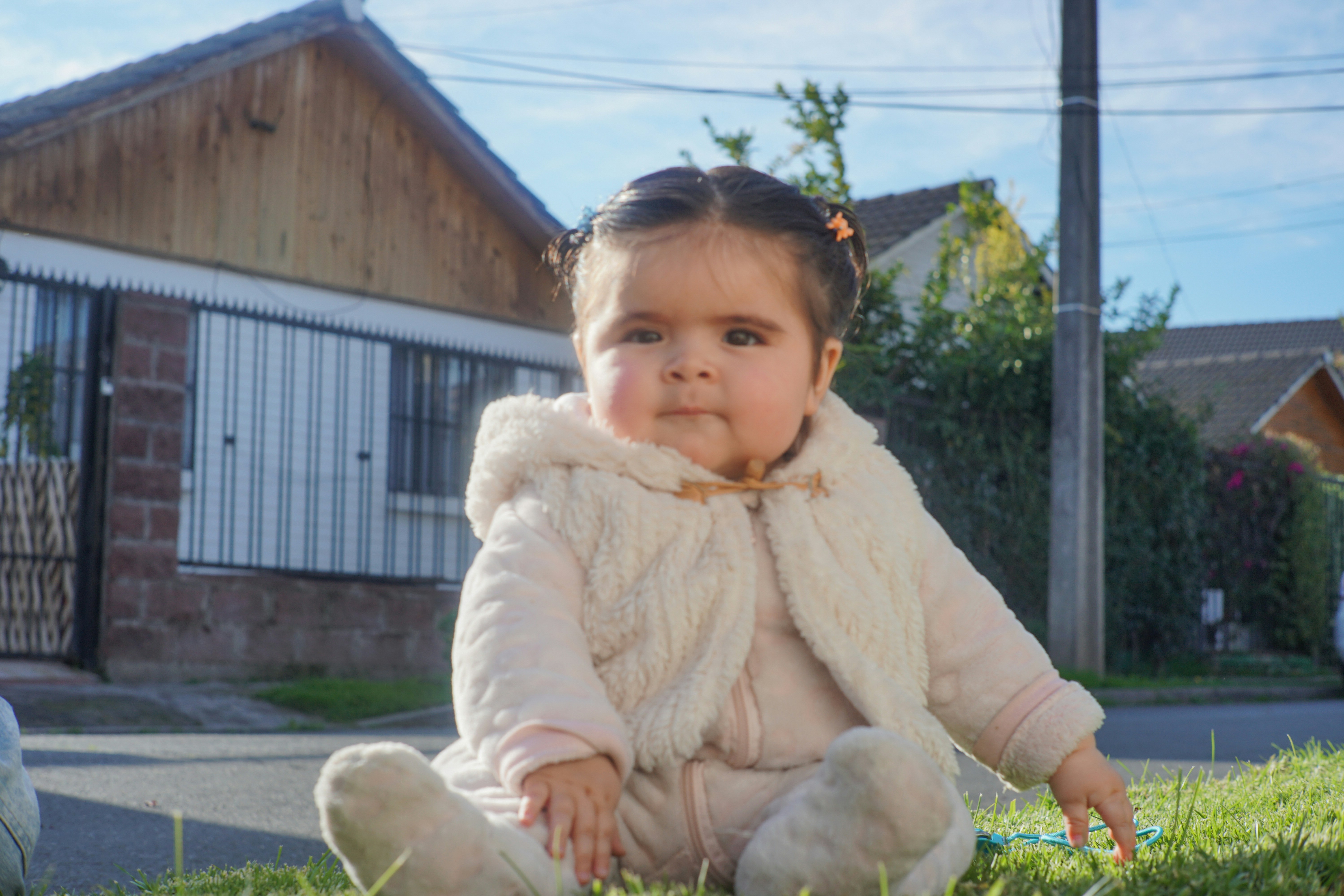 A cute baby girl sits outside on the grass.