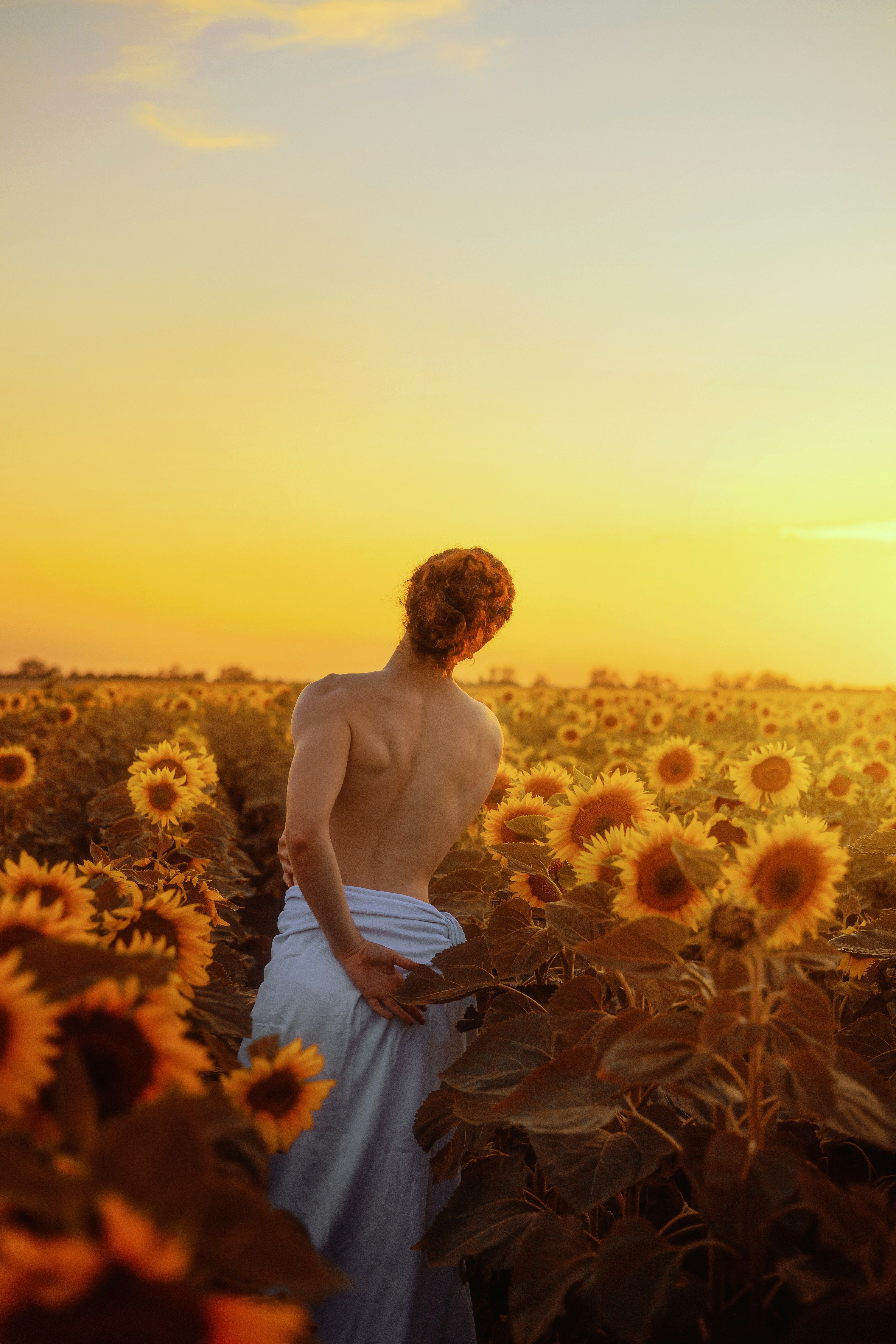 Mulher fica entre girassóis ao pôr do sol.