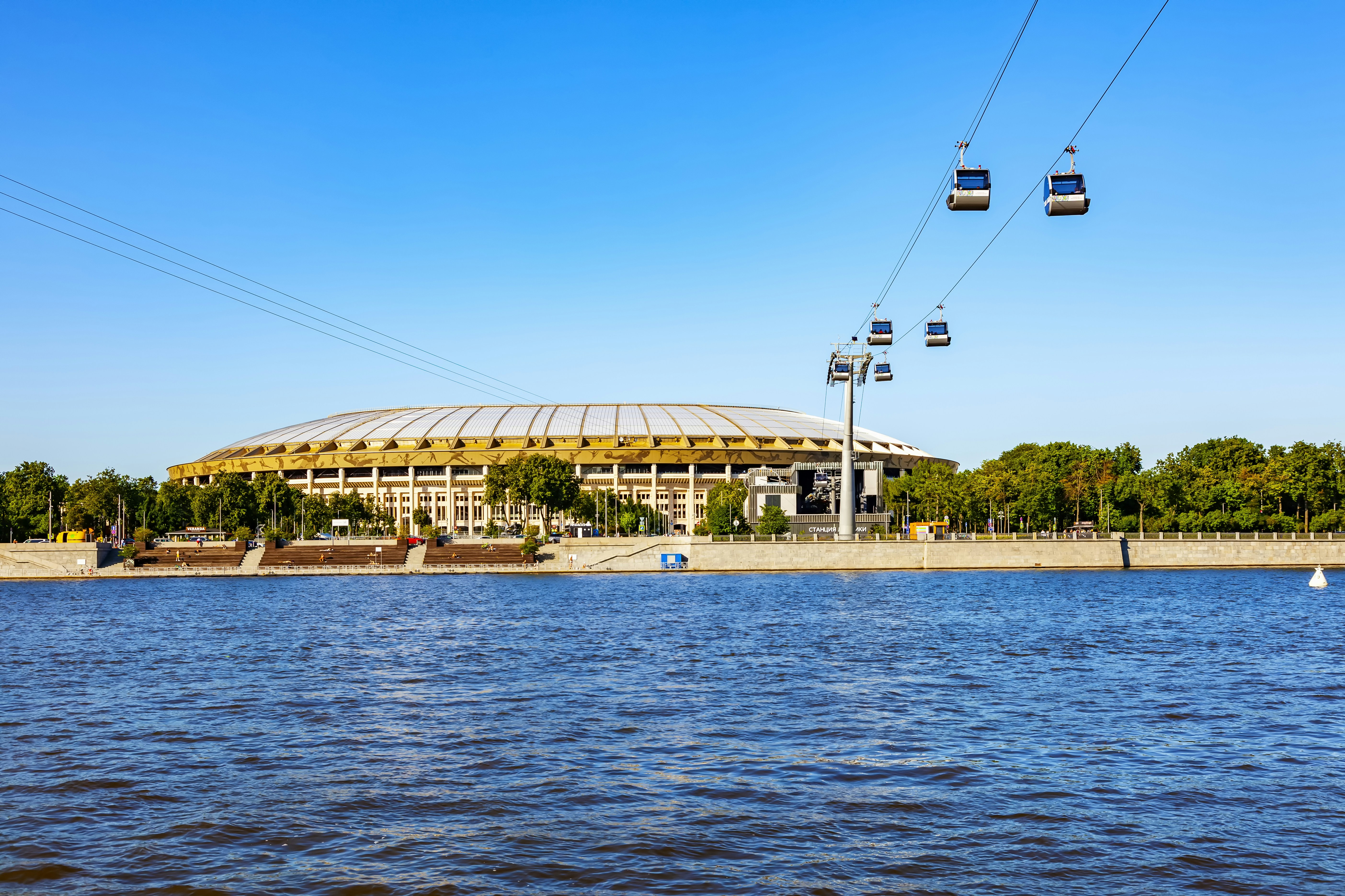 Cable cars travel over water near a stadium.