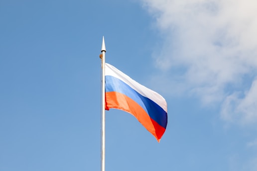 The russian flag waves against a blue sky.